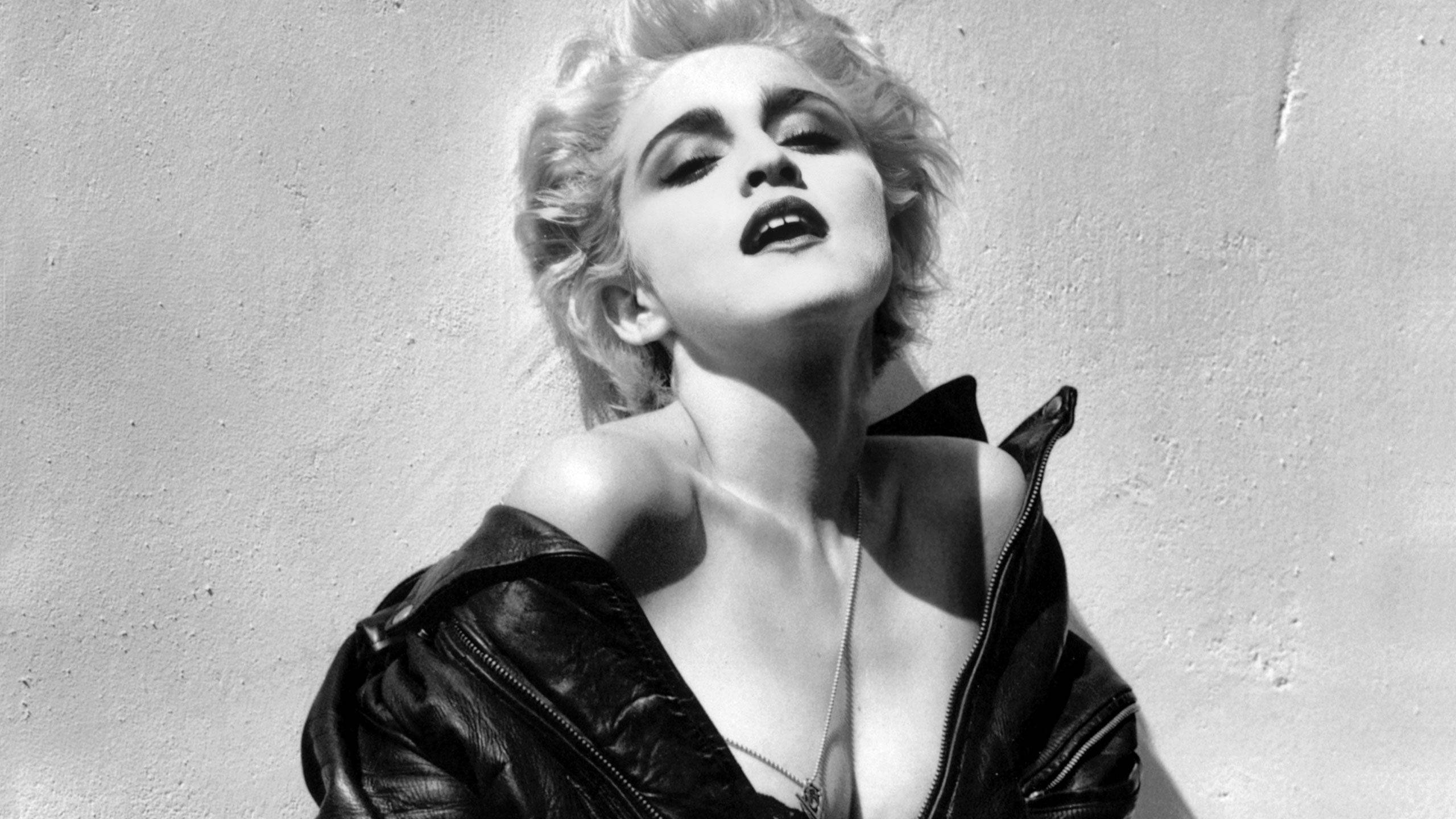Madonna 桌布 壁紙 — 一個引人注目的黑白肖像，一位金髮凌亂的女子穿著敞開的皮夾克，靠著素牆。