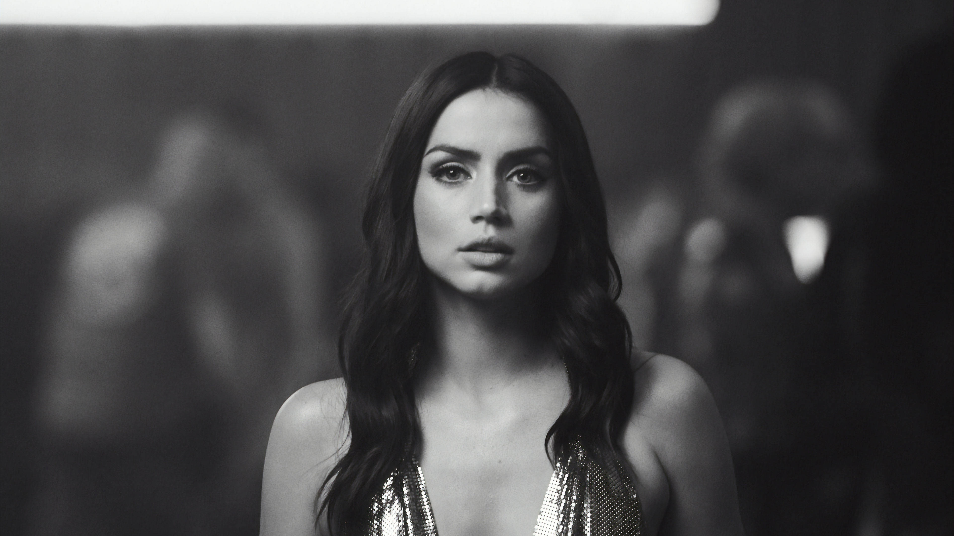 ana de armas 桌布 壁紙 — 一個引人注目的黑白肖像，一位長著深色長髮的女性穿著閃亮上衣，在昏暗模糊的背景中專注地凝視相機。