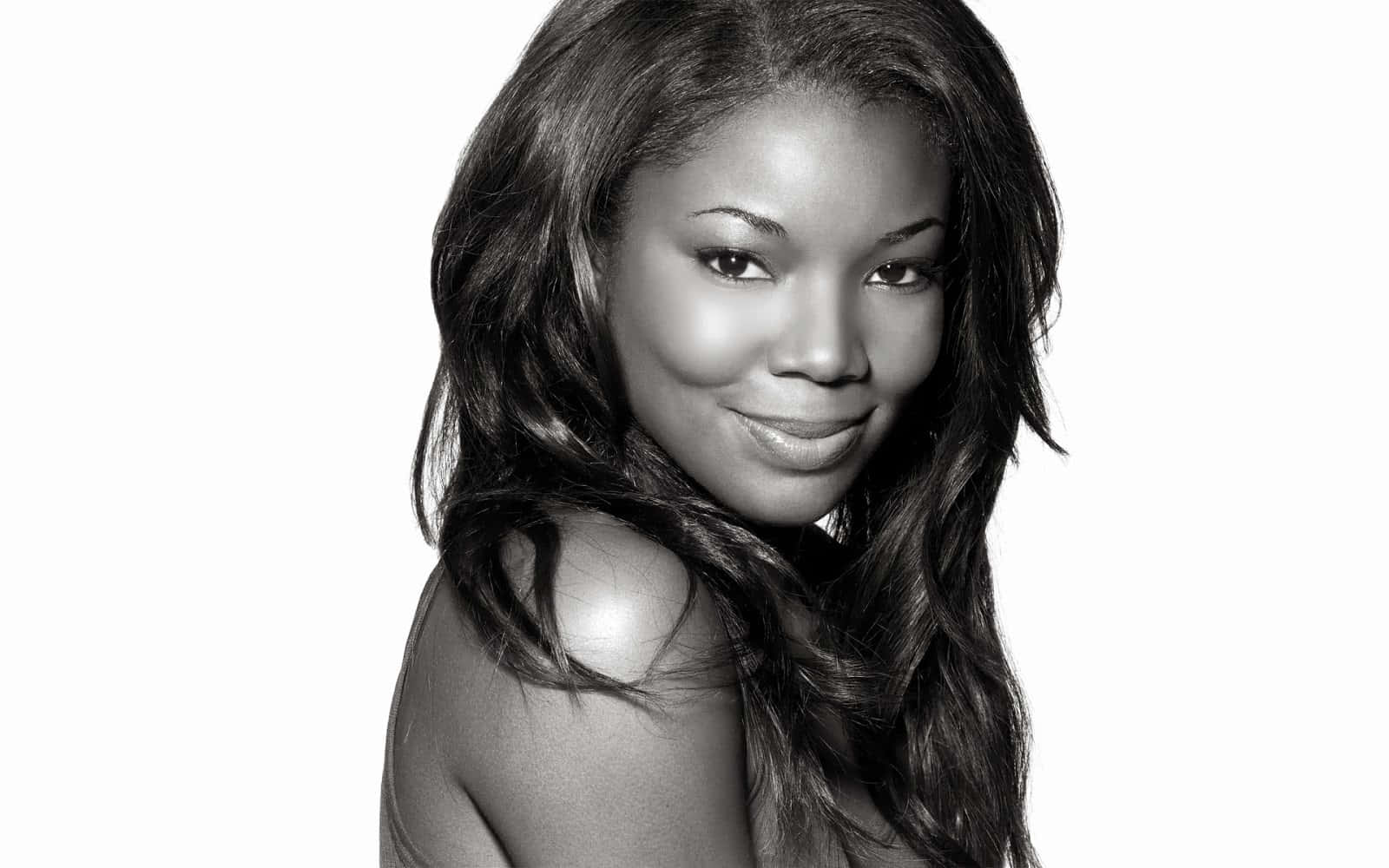 gabrielle union 桌布 壁紙 — 一個引人注目的黑白肖像，一位長著長波浪髮的女性在純白背景上溫柔微笑。