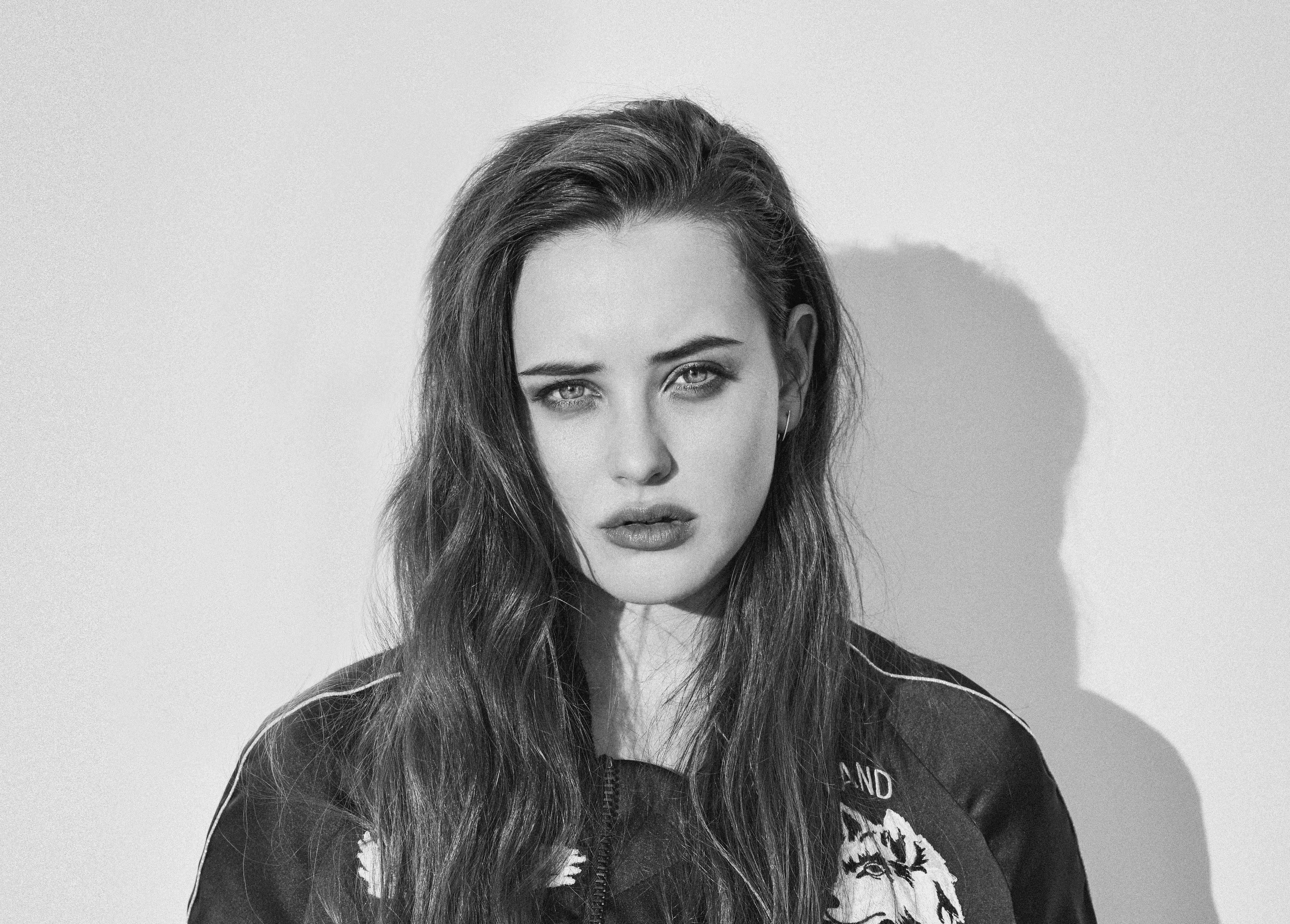 Katherine Langford 桌布 壁紙 — 一個引人注目的黑白肖像，一位長髮女性，眼神強烈，背景是樸素的牆壁，帶有戲劇性的陰影。
