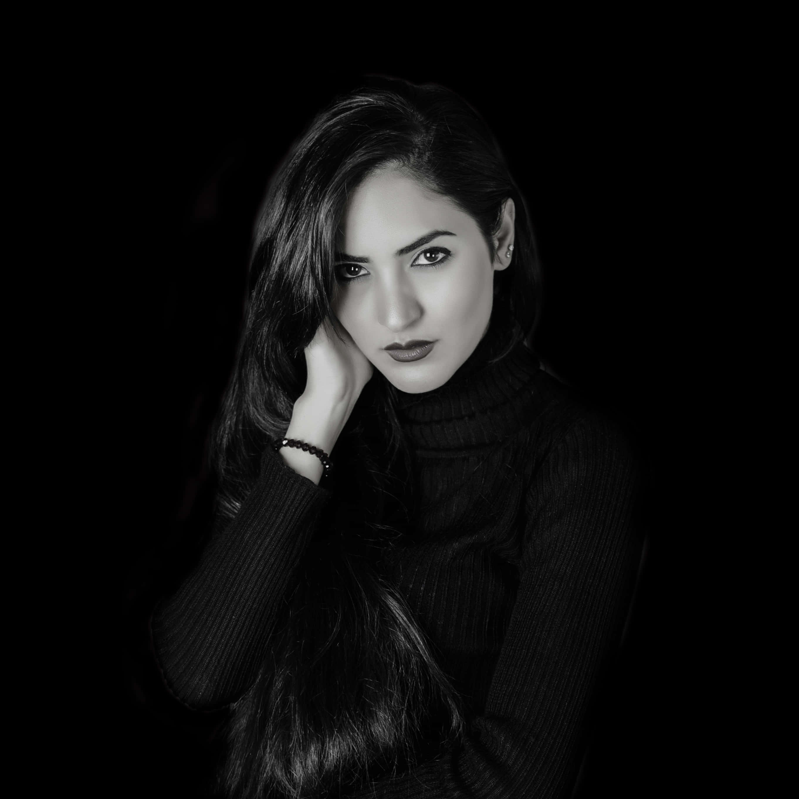 Woman 桌布 壁紙 — 一個引人注目的黑白肖像，一位長黑髮女性將下巴擱在手上，背景為純黑色。