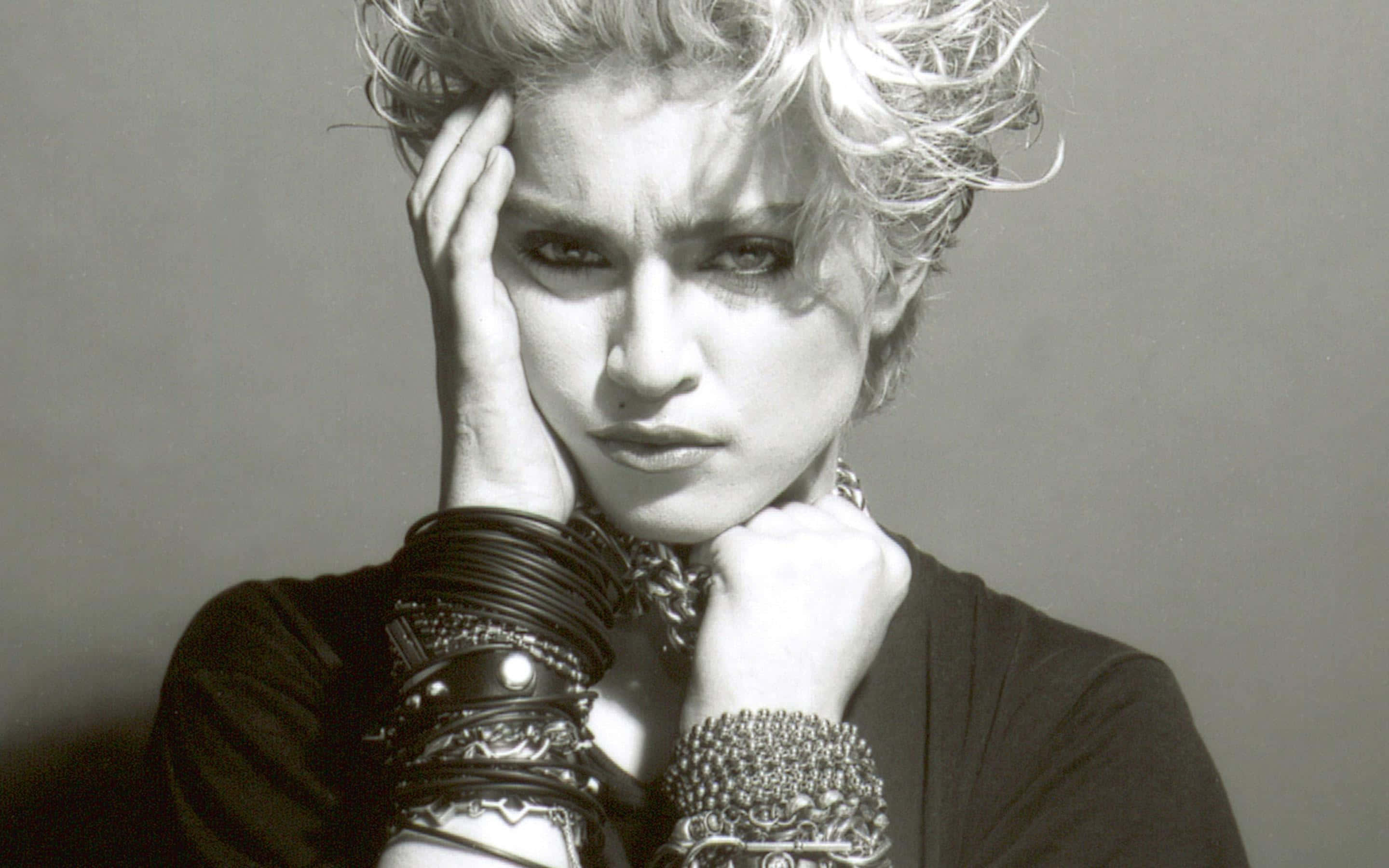 Madonna 桌布 壁紙 — 一個引人注目的黑白肖像，一位頭髮蓬亂、眼神強烈的女性，佩戴著厚重的層疊手鐲和項鍊。