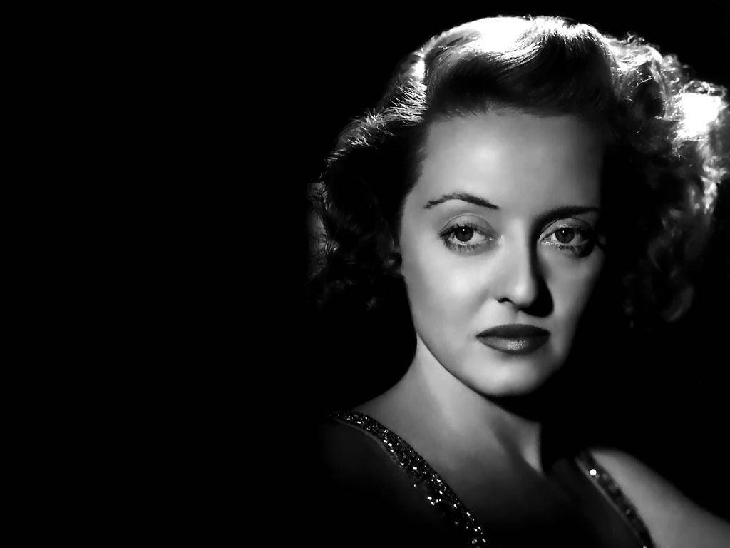 Bette Davis 桌布 壁紙 — 一個引人注目的黑白肖像，一位魅力女性，捲髮和鮮明嘴唇，背景深色。