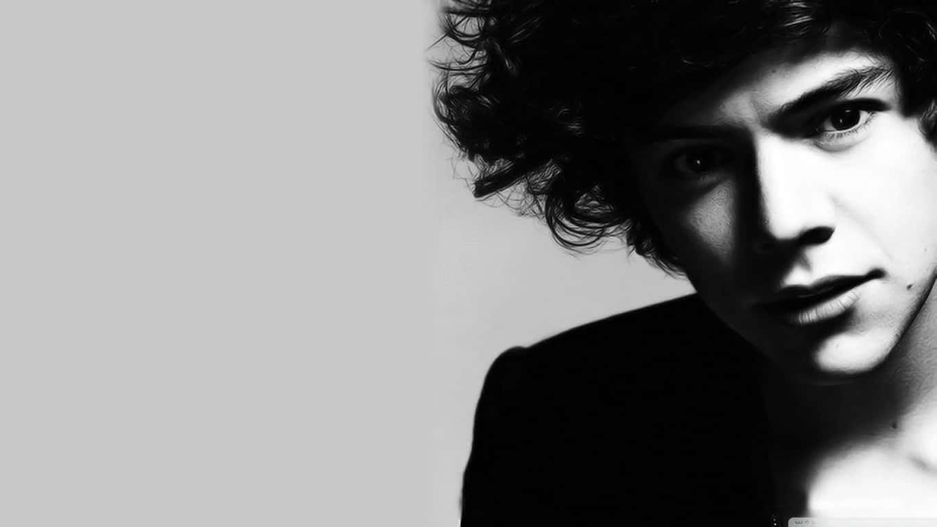 Harry Styles Black And White 桌布 壁紙 — 一個引人注目的黑白肖像，一個頭髮蓬亂的年輕男子在純色背景下專注地凝視。