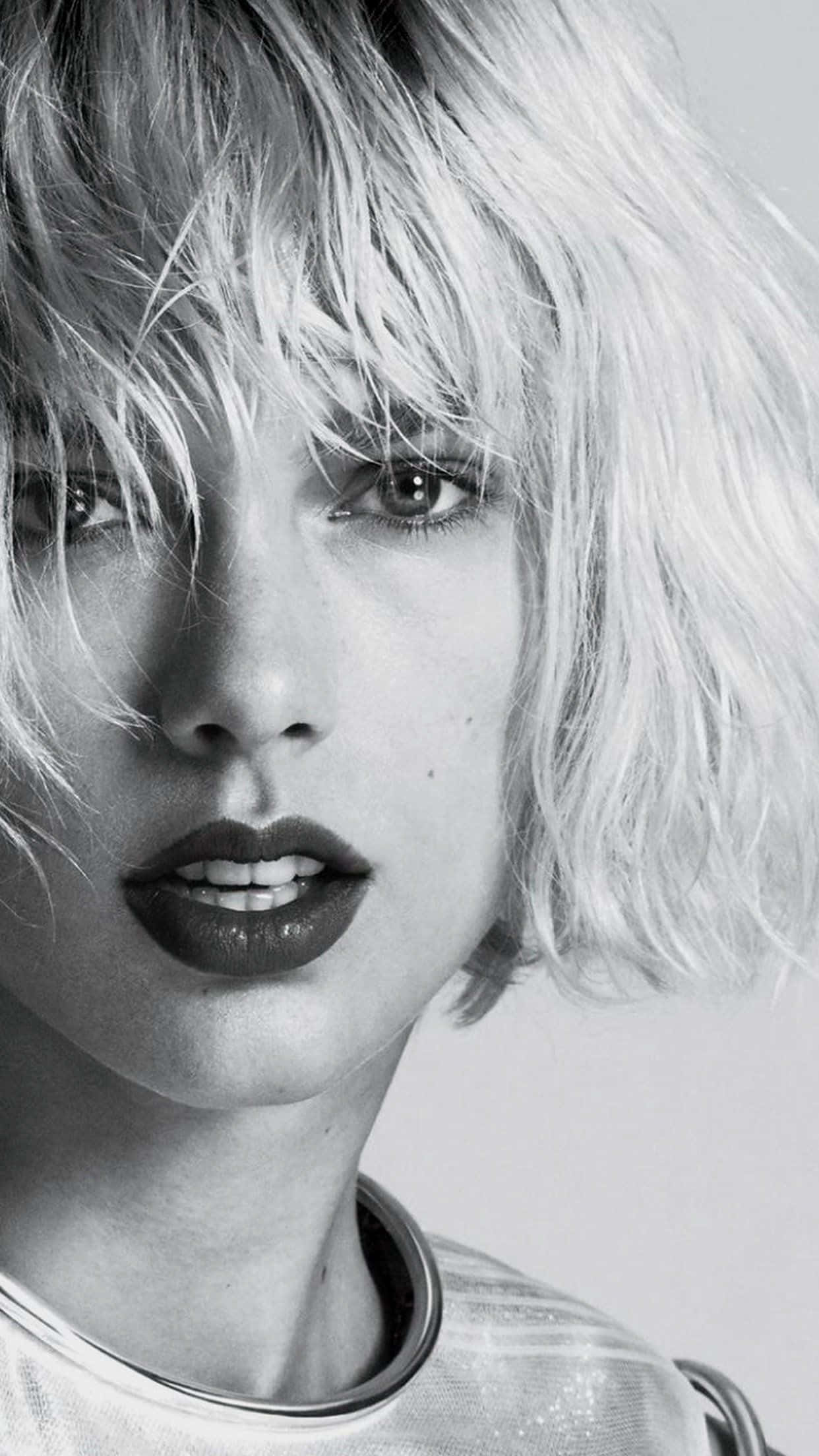 Taylor Swift iPhone 桌布 壁紙 — 一個引人注目的黑白肖像，拍攝一位頭髮蓬鬆的金髮女郎，嘴唇大膽，凝視著鏡頭。