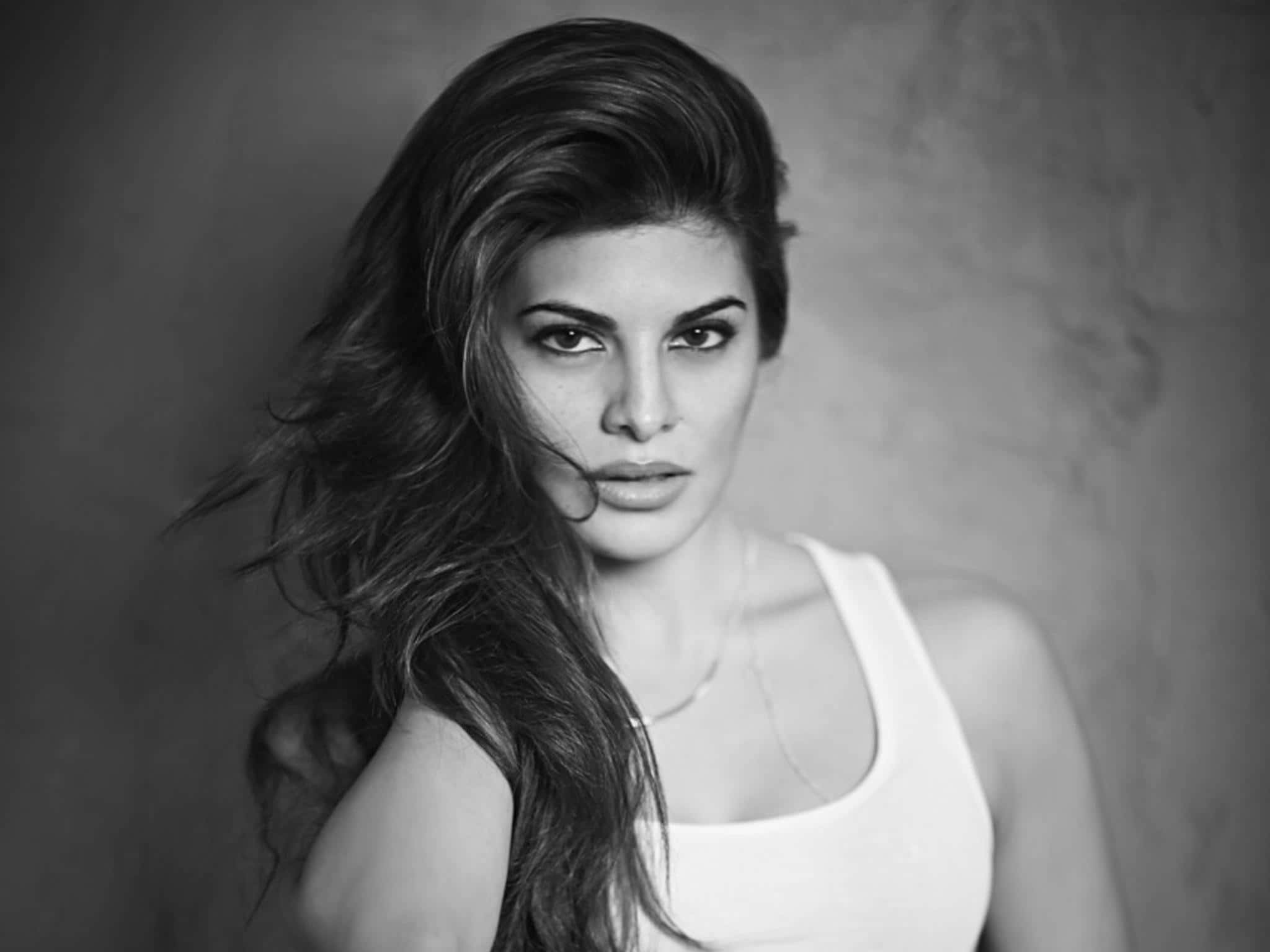 Jacqueline Fernandez 桌布 壁紙 — 一個引人注目的黑白肖像，捕捉一位頭髮被風吹拂、凝視鏡頭的女性。