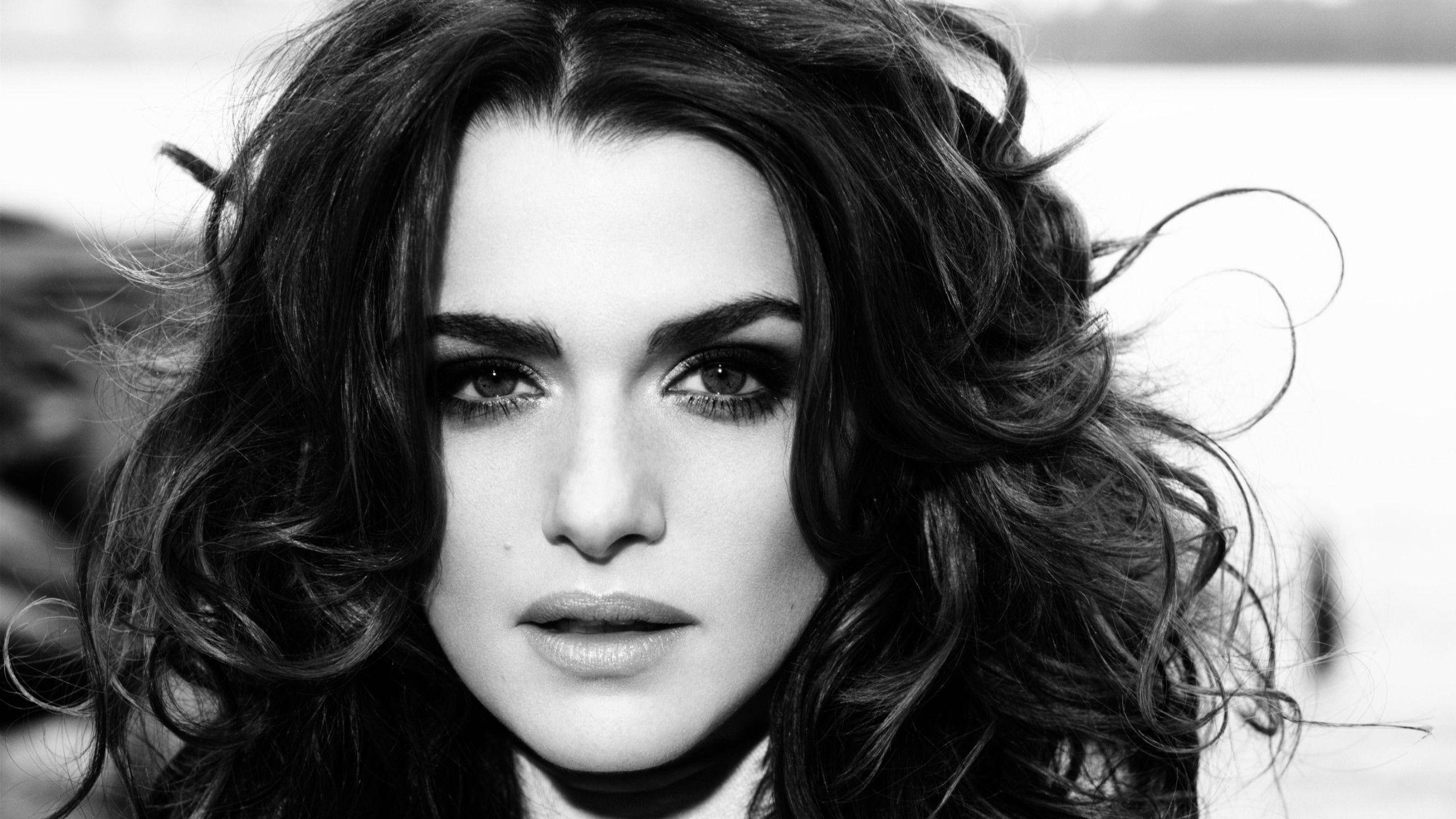 Rachel Weisz 桌布 壁紙 — 一個引人注目的黑白肖像，描繪一位擁有隨風飄揚的捲髮和強烈眼神直視觀眾的女性。