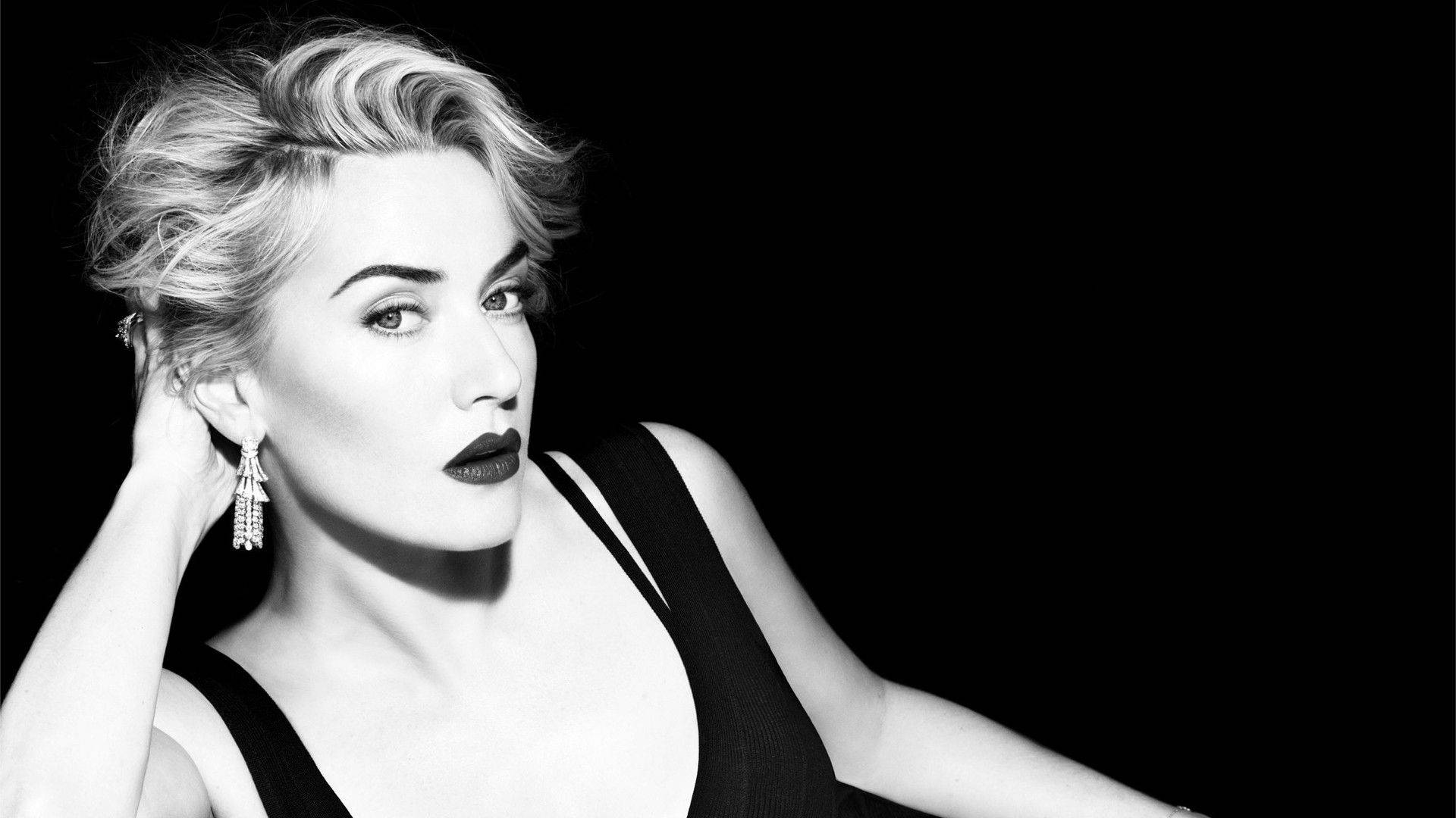 Kate Winslet 桌布 壁紙 — 一個引人注目的黑白肖像，描繪一位化著大膽妝容、戴著優雅耳環的女性，背景為深色。
