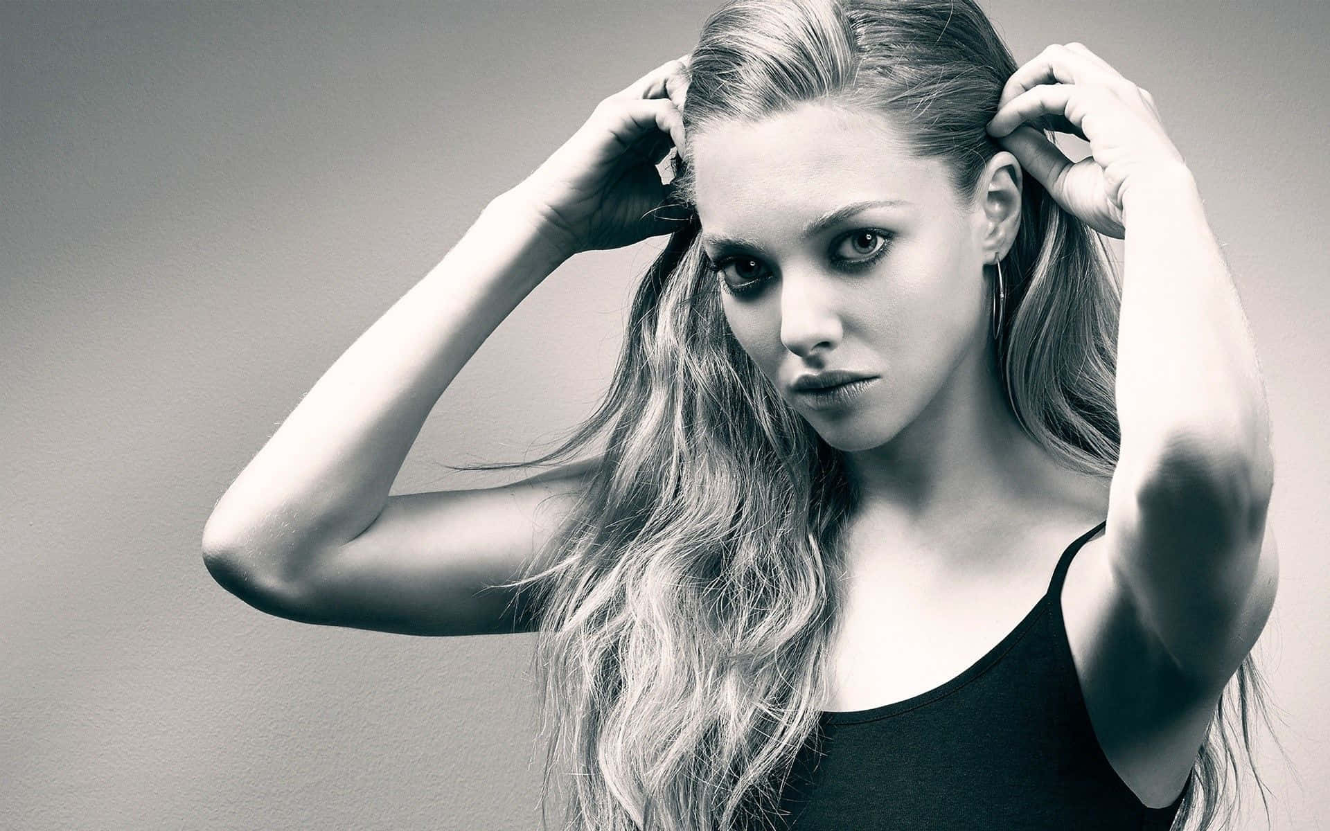 Amanda Seyfried 桌布 壁紙 — 一個引人注目的黑白肖像，長髮女性在調整頭髮時，眼神強烈地注視著相機。