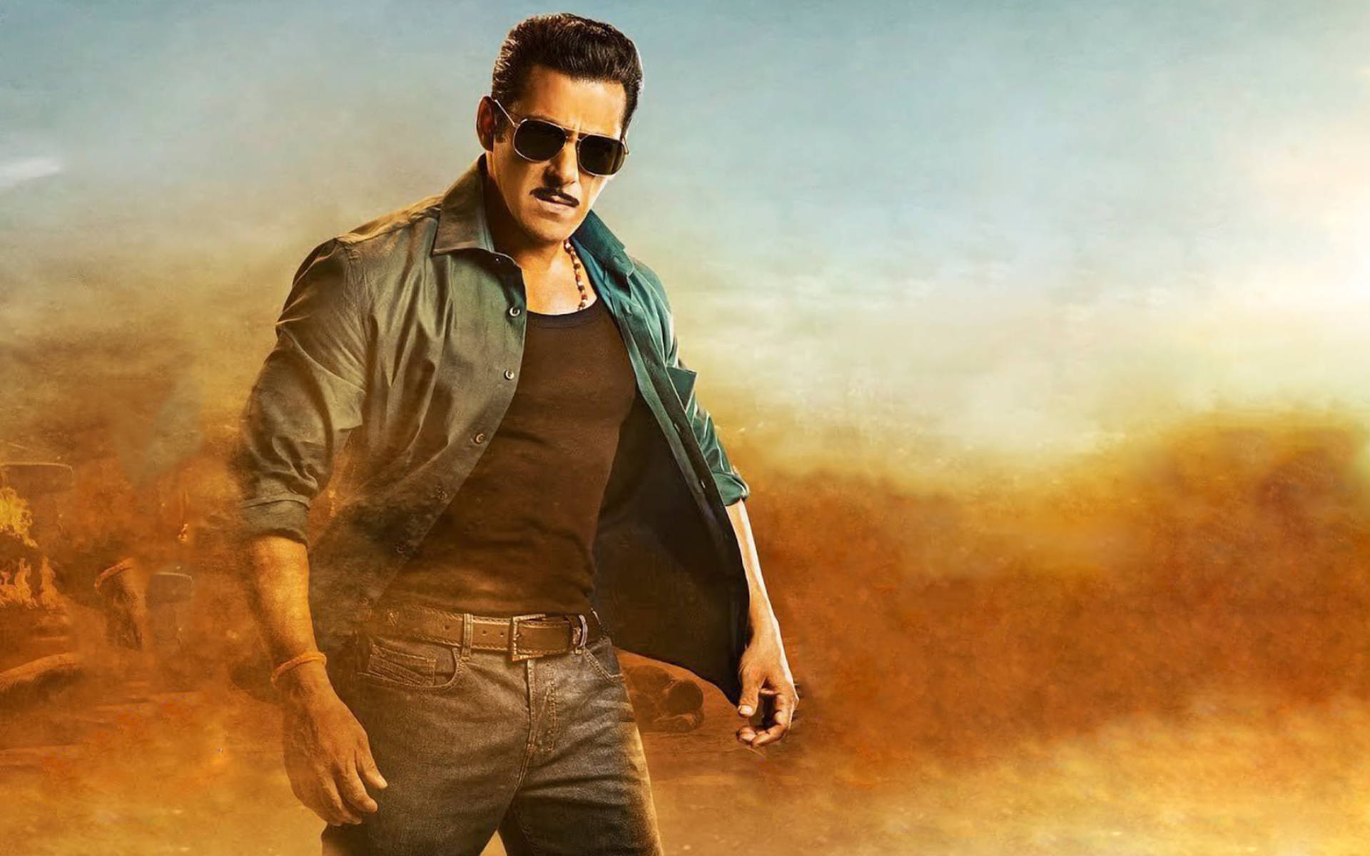 Salman Khan 桌布 壁紙 — 一個強壯的男人戴著太陽眼鏡和牛仔布，在塵土飛揚的沙漠景觀中自信地站立，天空朦朧。