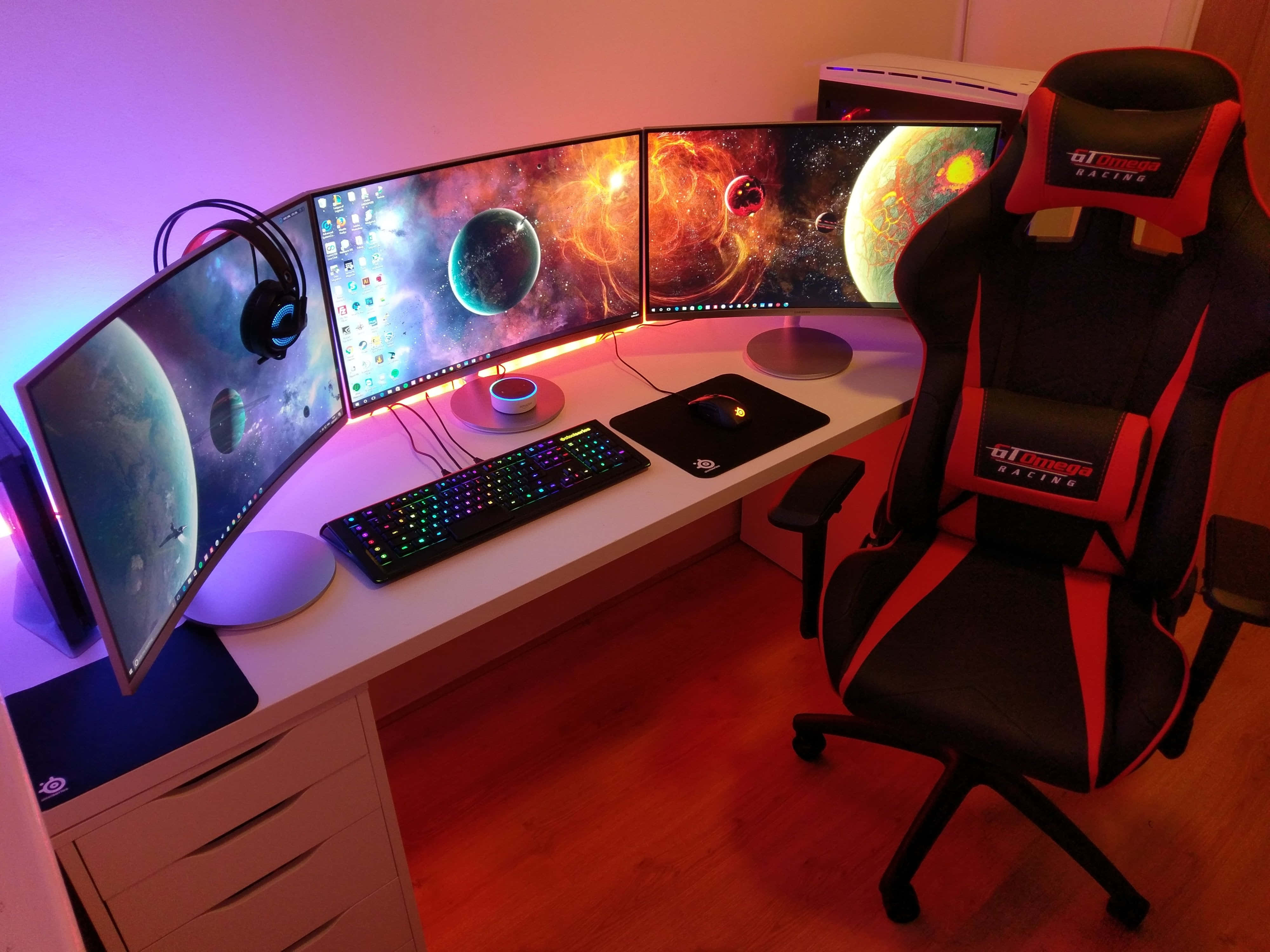 Gaming Pc Setup 桌布 壁紙 — 一個彎曲多顯示器遊戲設置，帶有宇宙壁紙，在環境RGB燈光下發光，旁邊是黑色和紅色的賽車椅。