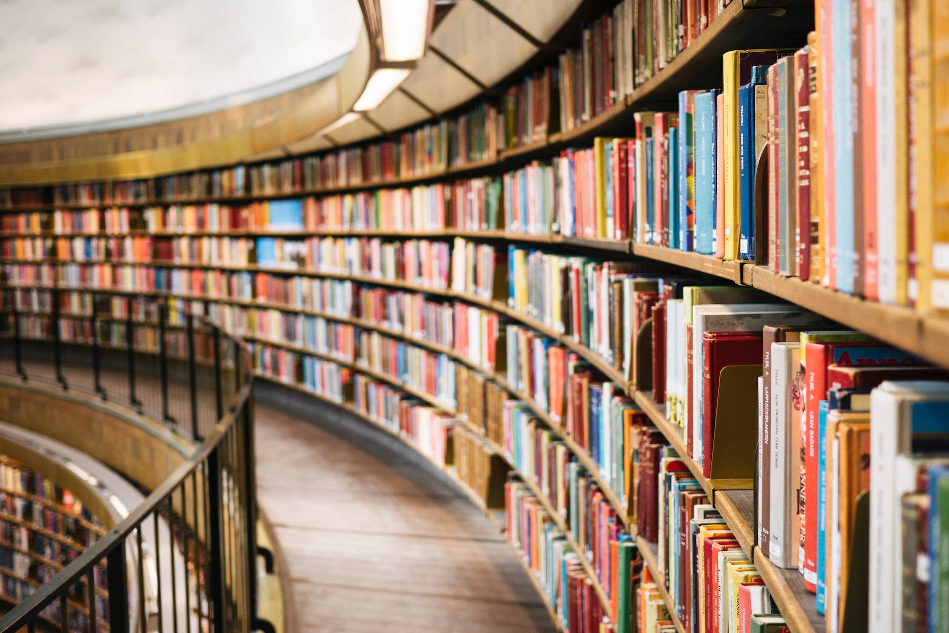 Library 桌布 壁紙 — 一個彎曲的木書架上放滿了色彩繽紛的書籍，在寧靜的圖書館中延伸至遠方。