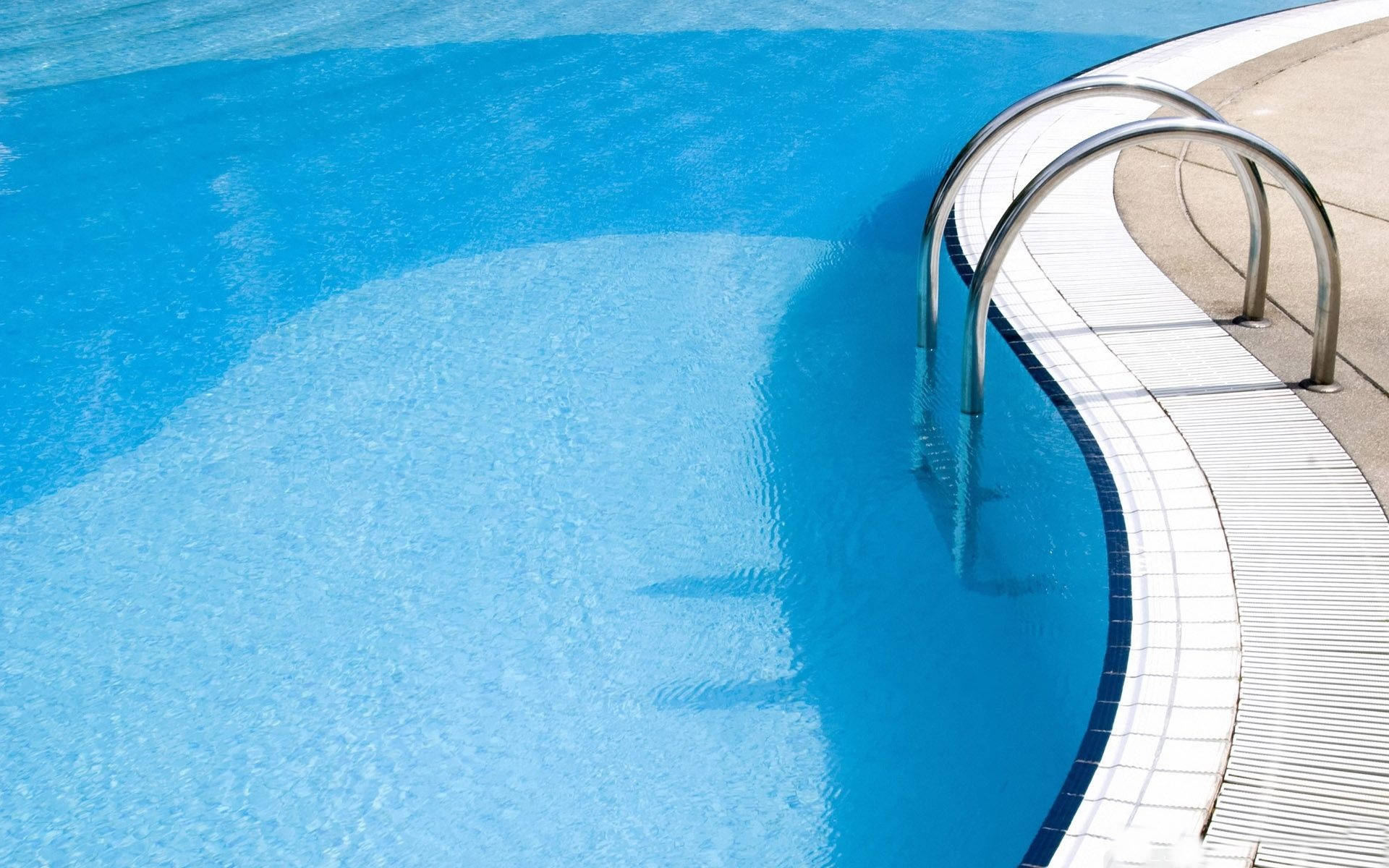 Swimming 桌布 壁紙 — 一個彎曲的游泳池，有清澈的藍色水和一個不鏽鋼梯子，在明亮的陽光下。