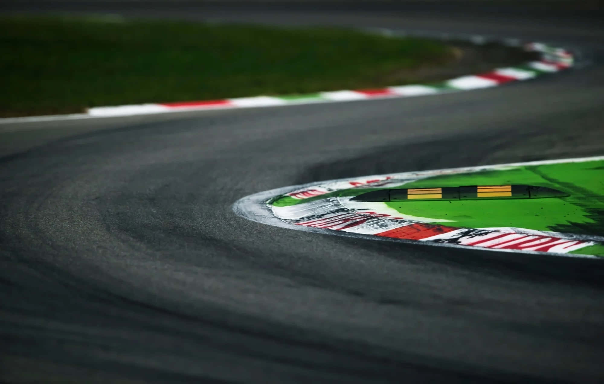 Race Track 桌布 壁紙 — 一個彎曲的瀝青賽道彎角的特寫，帶有紅、白、綠三色路緣石和輪胎痕跡。