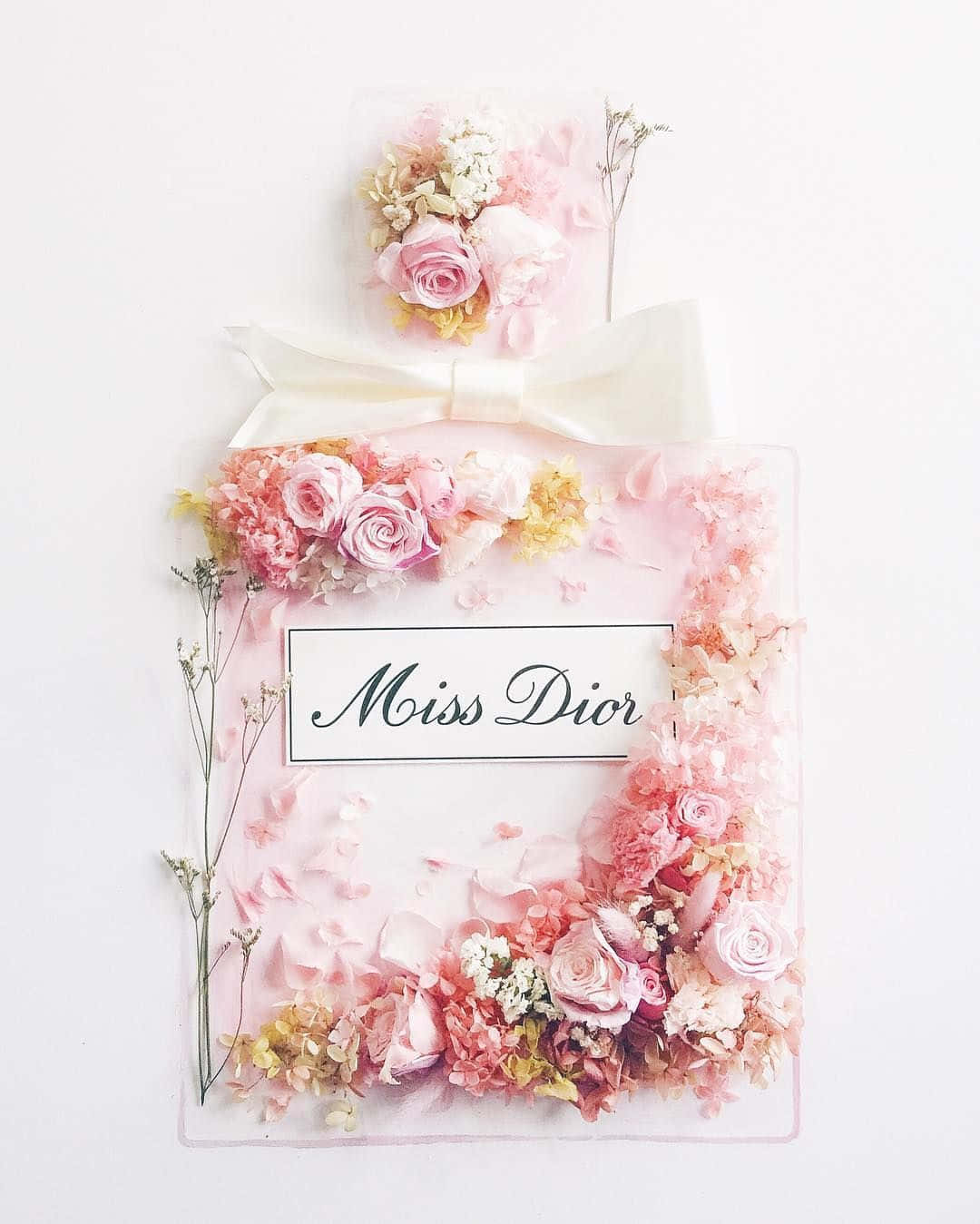 Dior 動態 桌布 壁紙 — 一個形狀像花卉佈置的香水瓶，帶有粉紅玫瑰和乾花，背景為白色。