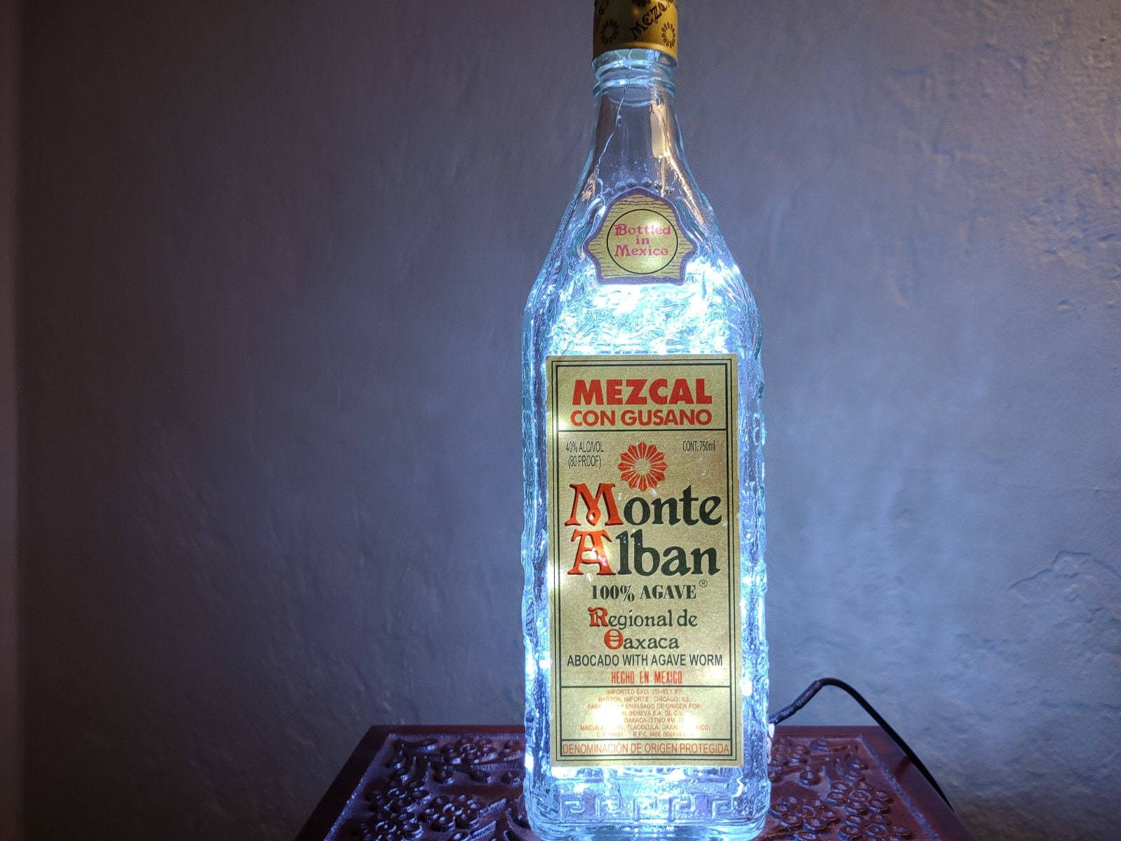 Drink 桌布 壁紙 — 一個從內部發光的 Monte Alban 梅斯卡爾酒瓶，向有紋理的牆壁投射藍光。