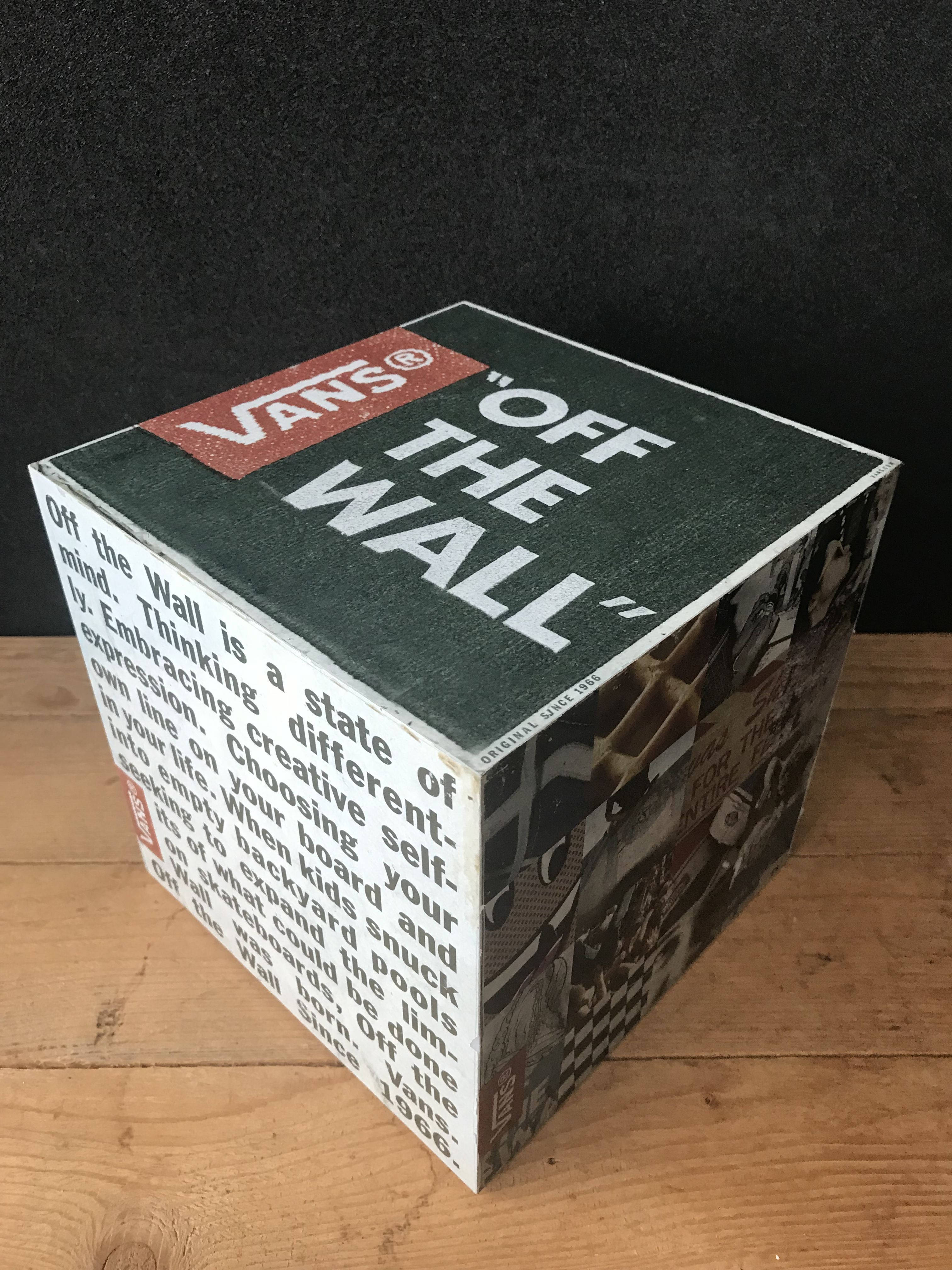 Vans Off The Wall 桌布 壁紙 — 一個復古 Vans 'Off The Wall' 品牌立方體，帶有文字和滑板圖案，放置在木質表面上，背景為深色。
