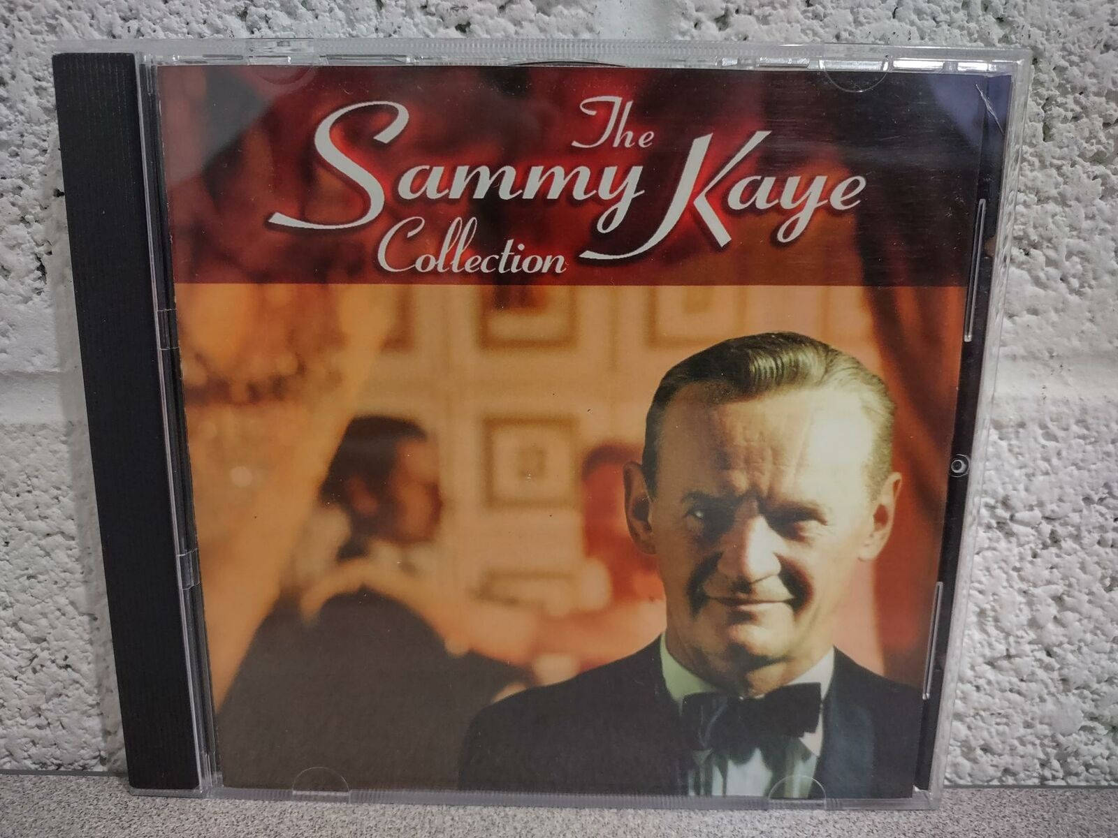 Album Cover 桌布 壁紙 — 一個復古CD盒，用於'The Sammy Kaye Collection'，展示一位微笑的男士穿著燕尾服，背景溫暖模糊。