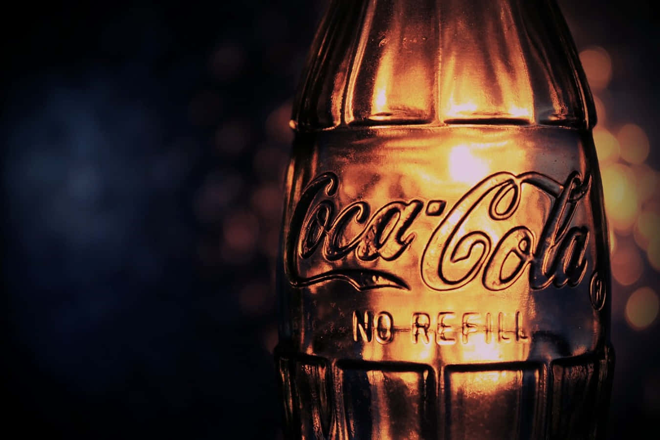 coca cola 桌布 壁紙 — 一個復古可口可樂玻璃瓶在帶有金色光反射的暗色散景背景下溫暖地發光。