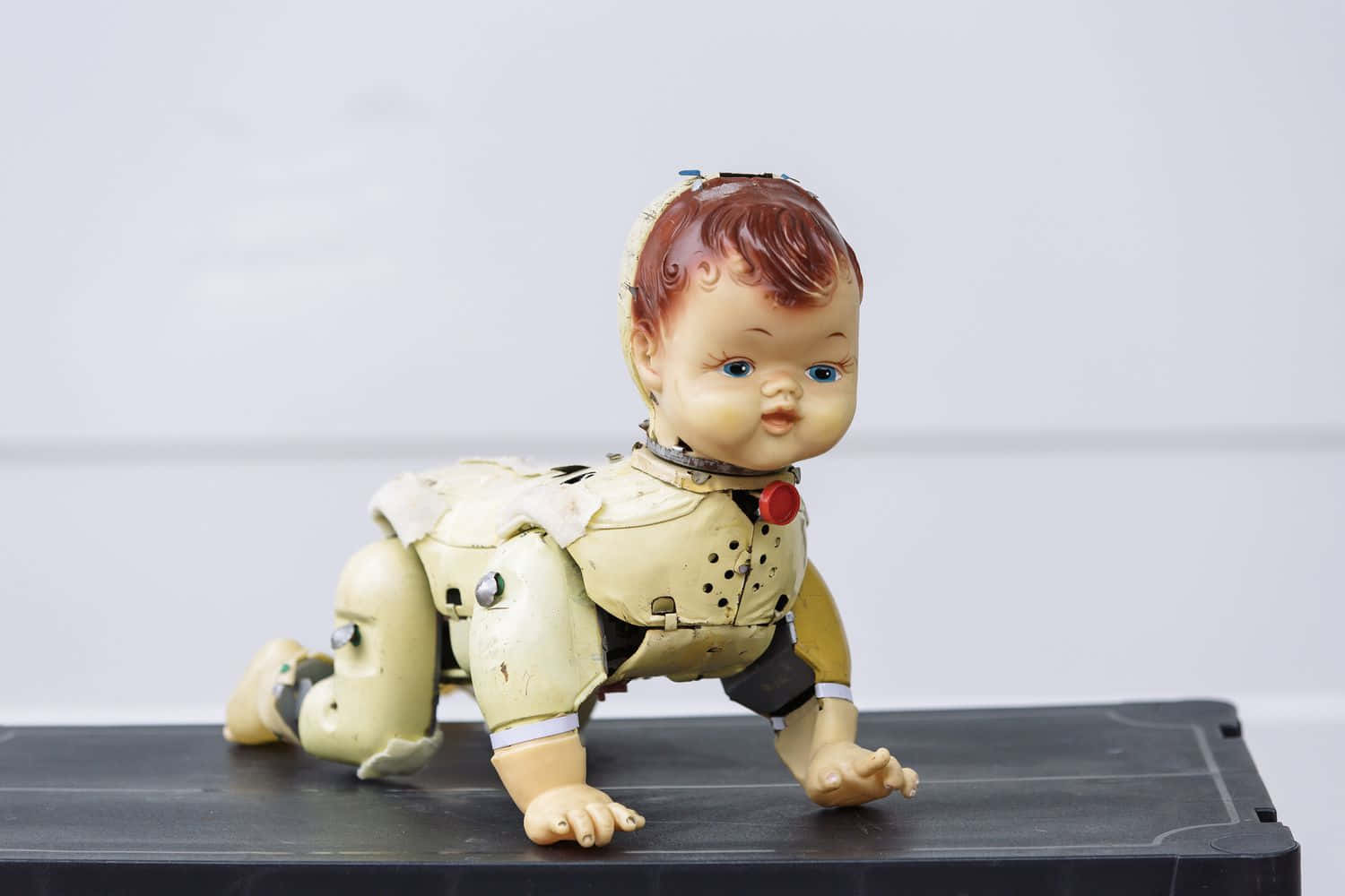 Dolls 桌布 壁紙 — 一個復古嬰兒娃娃，帶有暴露的機械關節和裂紋油漆，在黑色表面上爬行，背景為純白色。