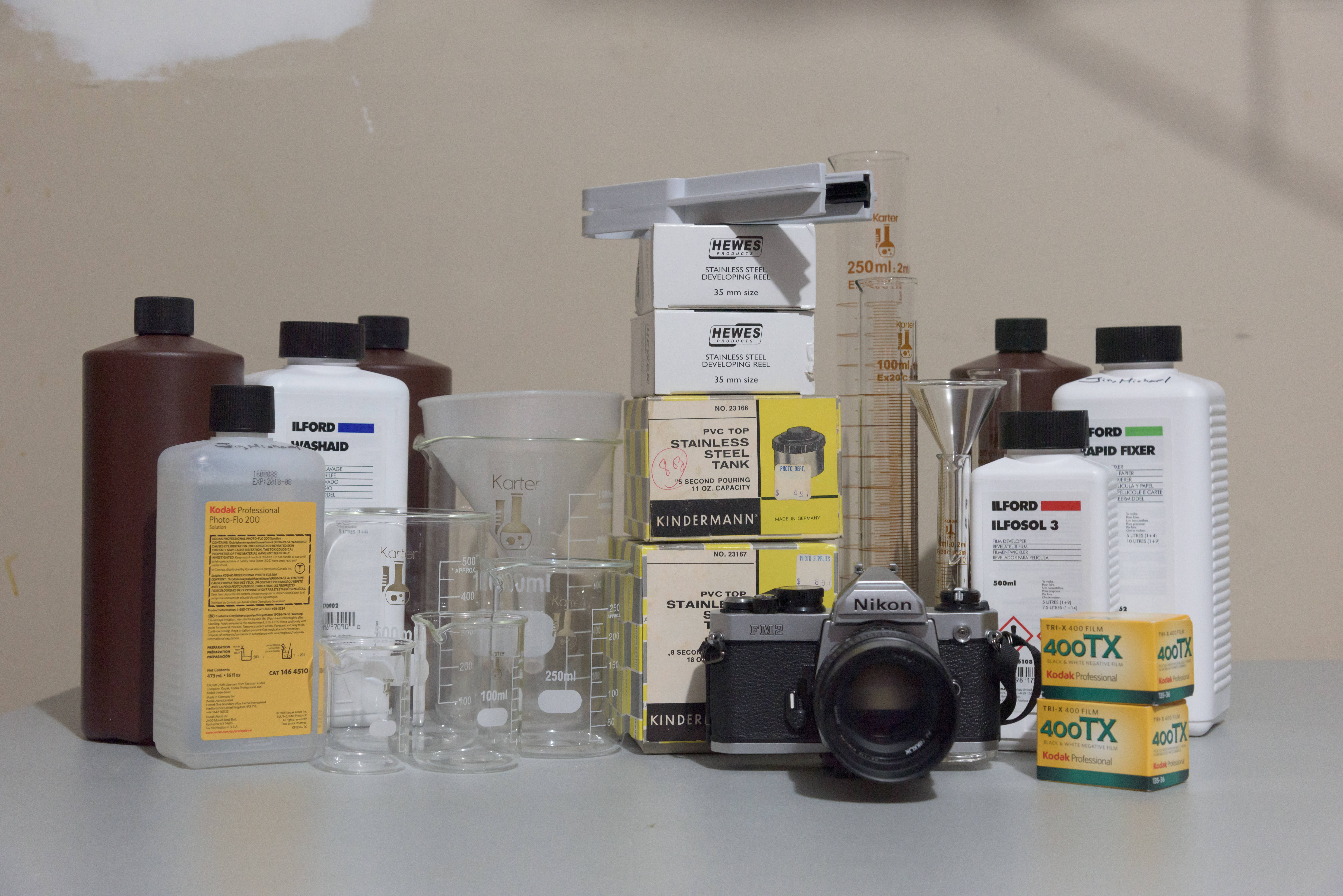 Beaker 桌布 壁紙 — 一個復古底片攝影設置，包括Nikon相機、化學品和玻璃器皿，排列在中性表面上。