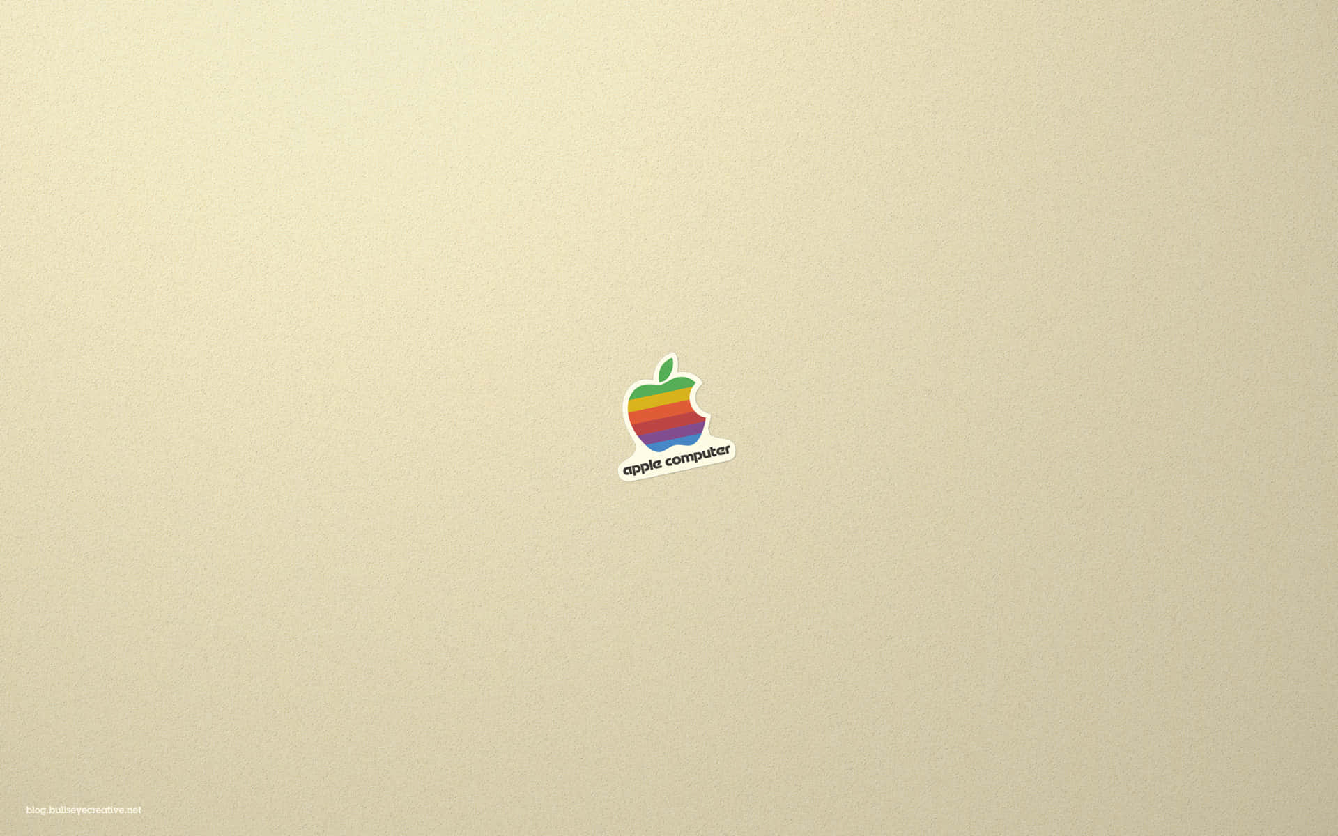 Old Mac 桌布 壁紙 — 一個復古彩虹Apple Computer標誌貼紙，置於帶有細微紋理的米色筆記型電腦蓋中央。