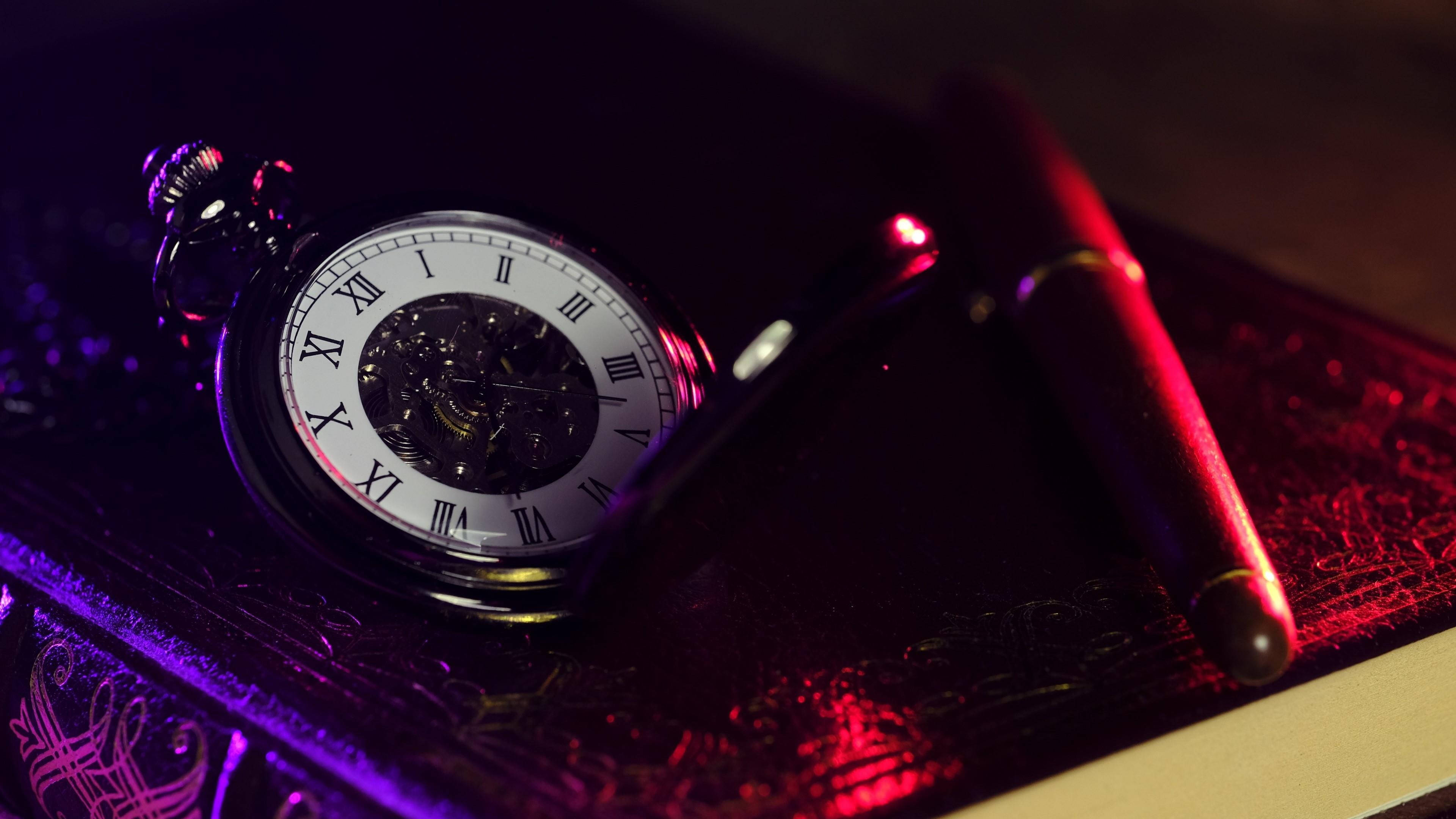 times up 桌布 壁紙 — 一個復古懷錶，帶有暴露的齒輪和一支紅色筆，放在一本華麗的書上，在戲劇性的紫色和紅色燈光下。