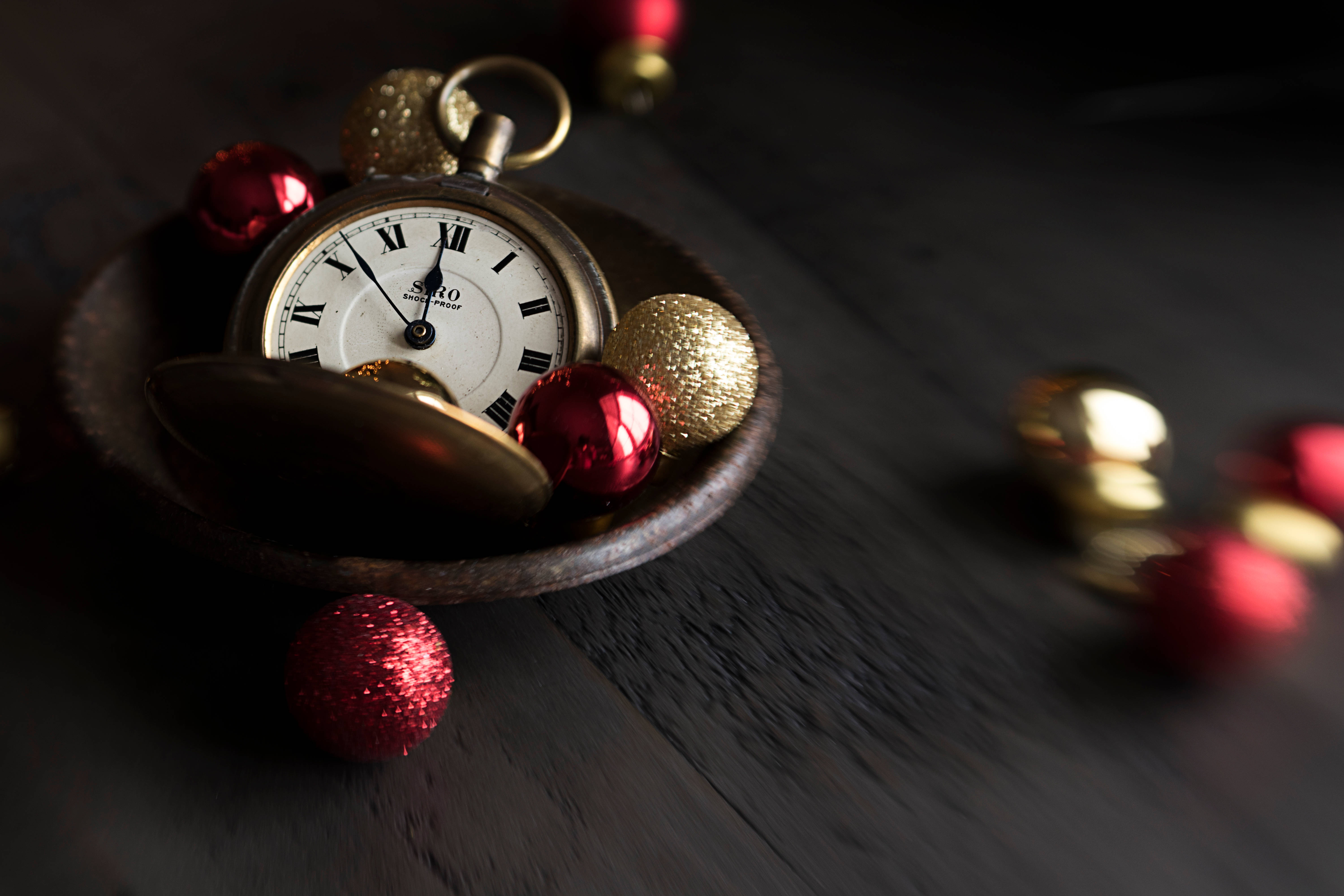 Time 桌布 壁紙 — 一個復古懷錶放在一個木碗中，周圍環繞著紅色和金色的聖誕裝飾品，置於深色木質表面上。
