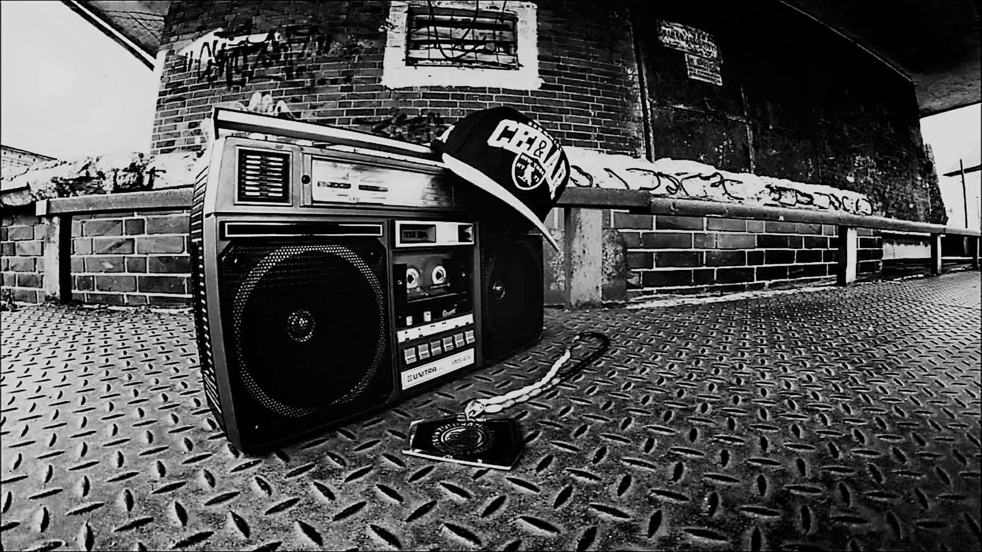 hiphop 桌布 壁紙 — 一個復古手提音箱和棒球帽放在有紋理的金屬地板上，背景是單色塗鴉磚牆。