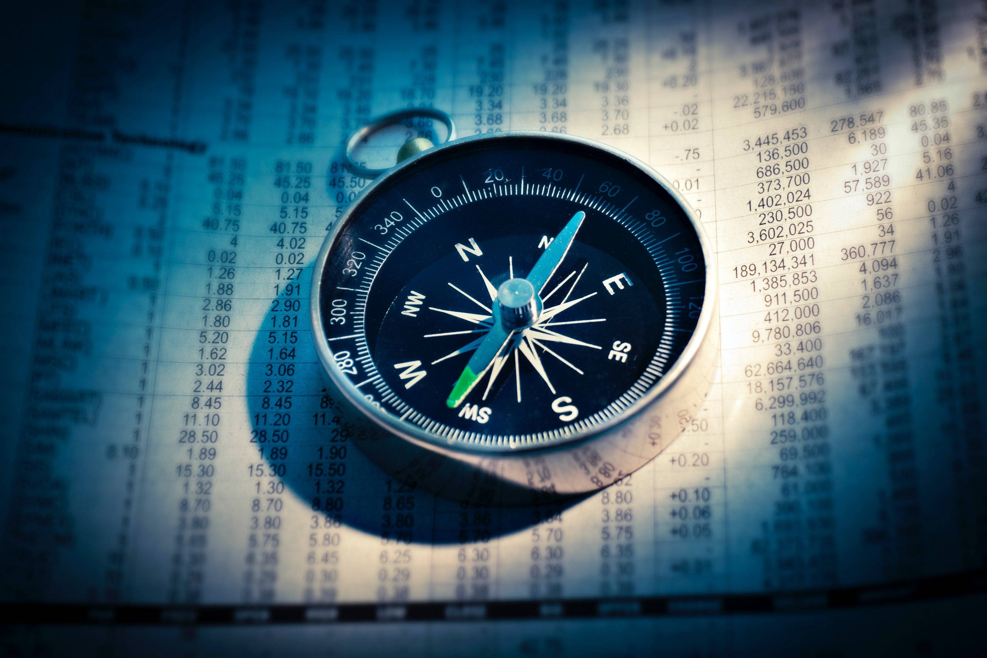 Market 桌布 壁紙 — 一個復古指南針放在一個帶有發光藍色數字和指向北方的箭頭的金融圖表上。