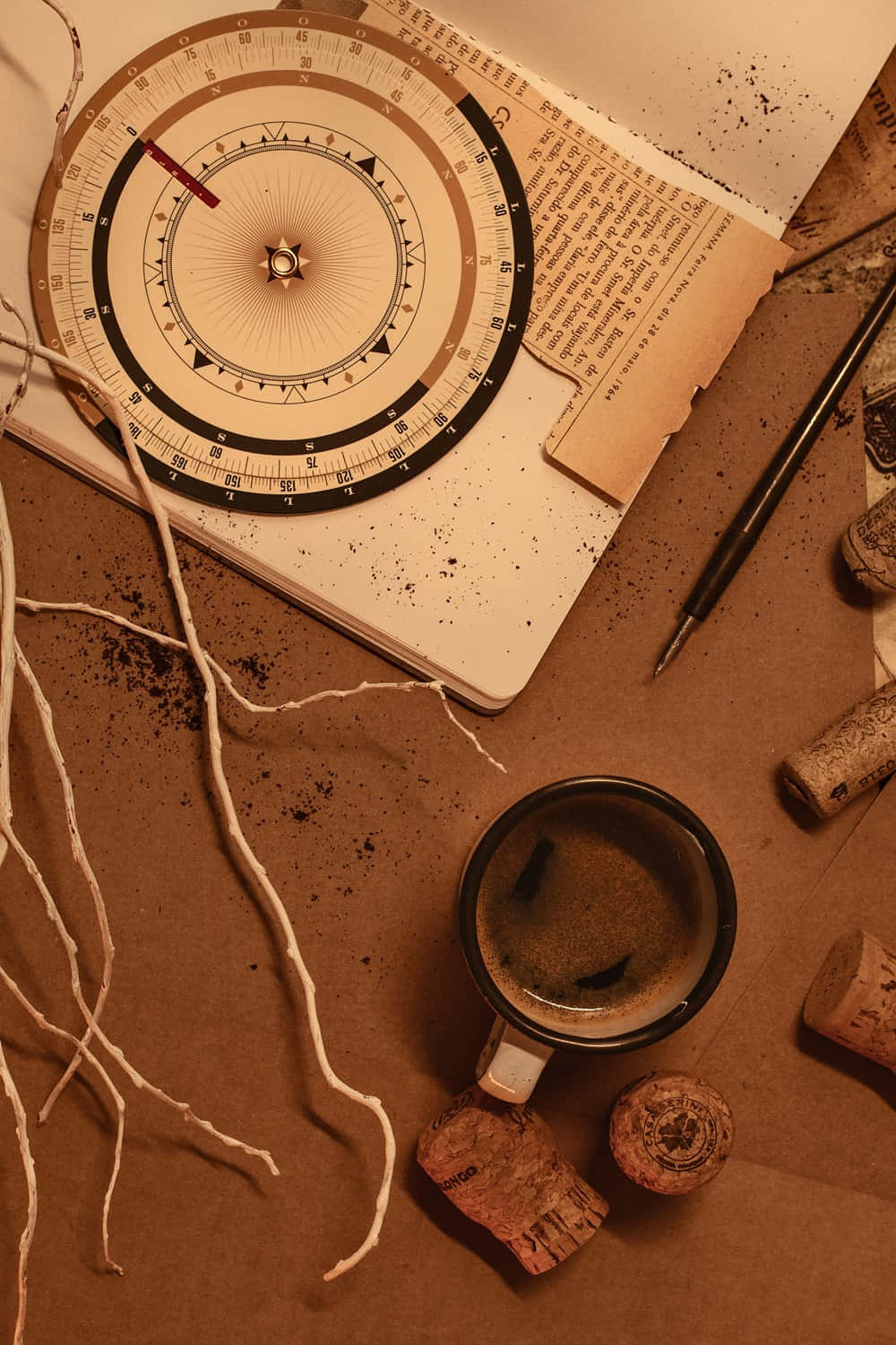 Soft Brown Aesthetic 桌布 壁紙 — 一個復古指南針放在打開的筆記本上，旁邊有冒煙的馬克杯和散落的軟木塞，在溫暖的棕褐色燈光下。