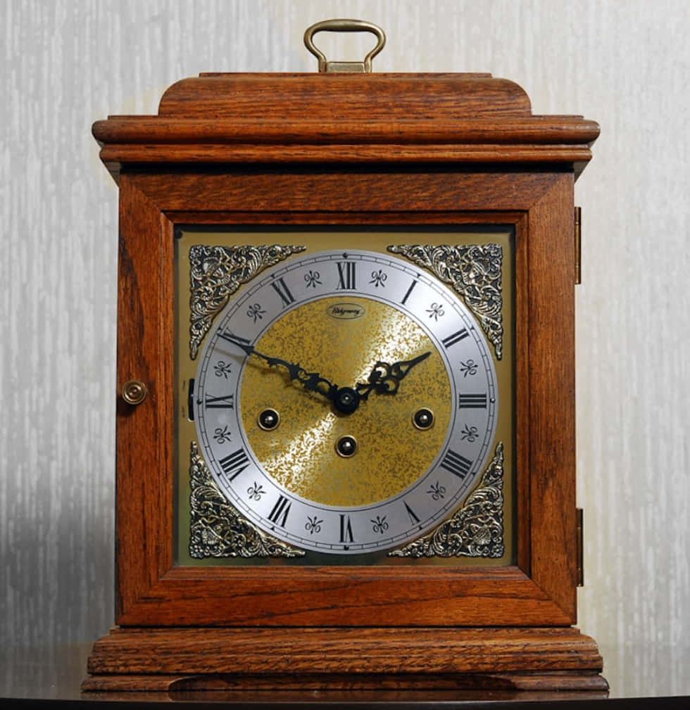 Clock 桌布 壁紙 — 一個復古木製掛鐘，帶有金色紋理錶面和華麗的銀色角落，靠在淺色條紋牆上。