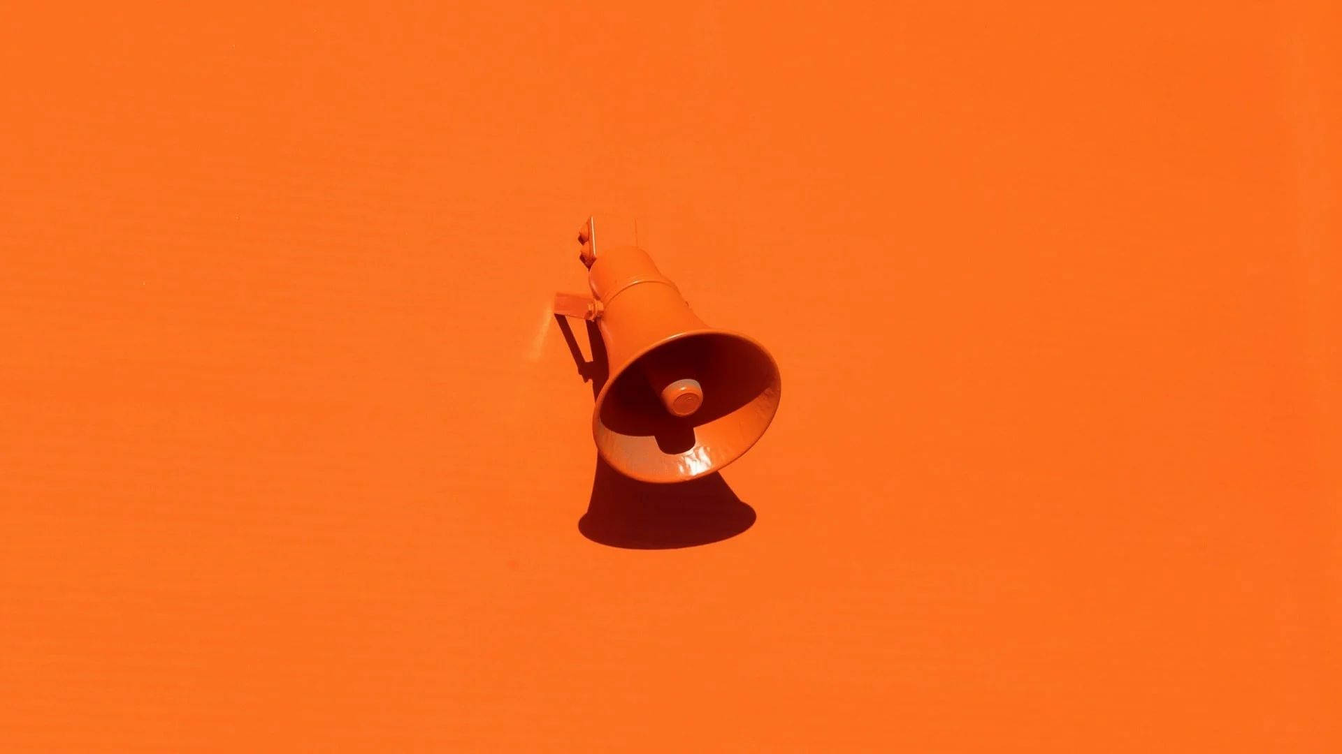 Orange 桌布 壁紙 — 一個復古橙色擴音器在明亮光線下，在純橙色牆壁上投射出清晰的陰影。