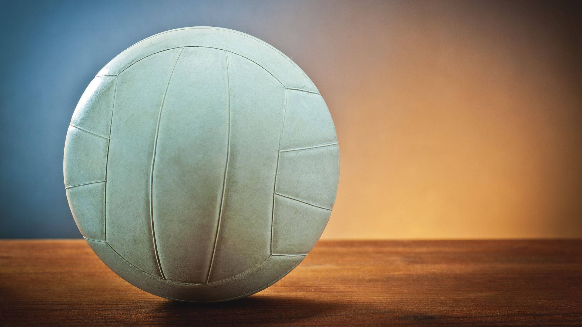 Volleyball Aesthetic 桌布 壁紙 — 一個復古白色排球放在木質表面上，背景是藍色到橙色的漸變。