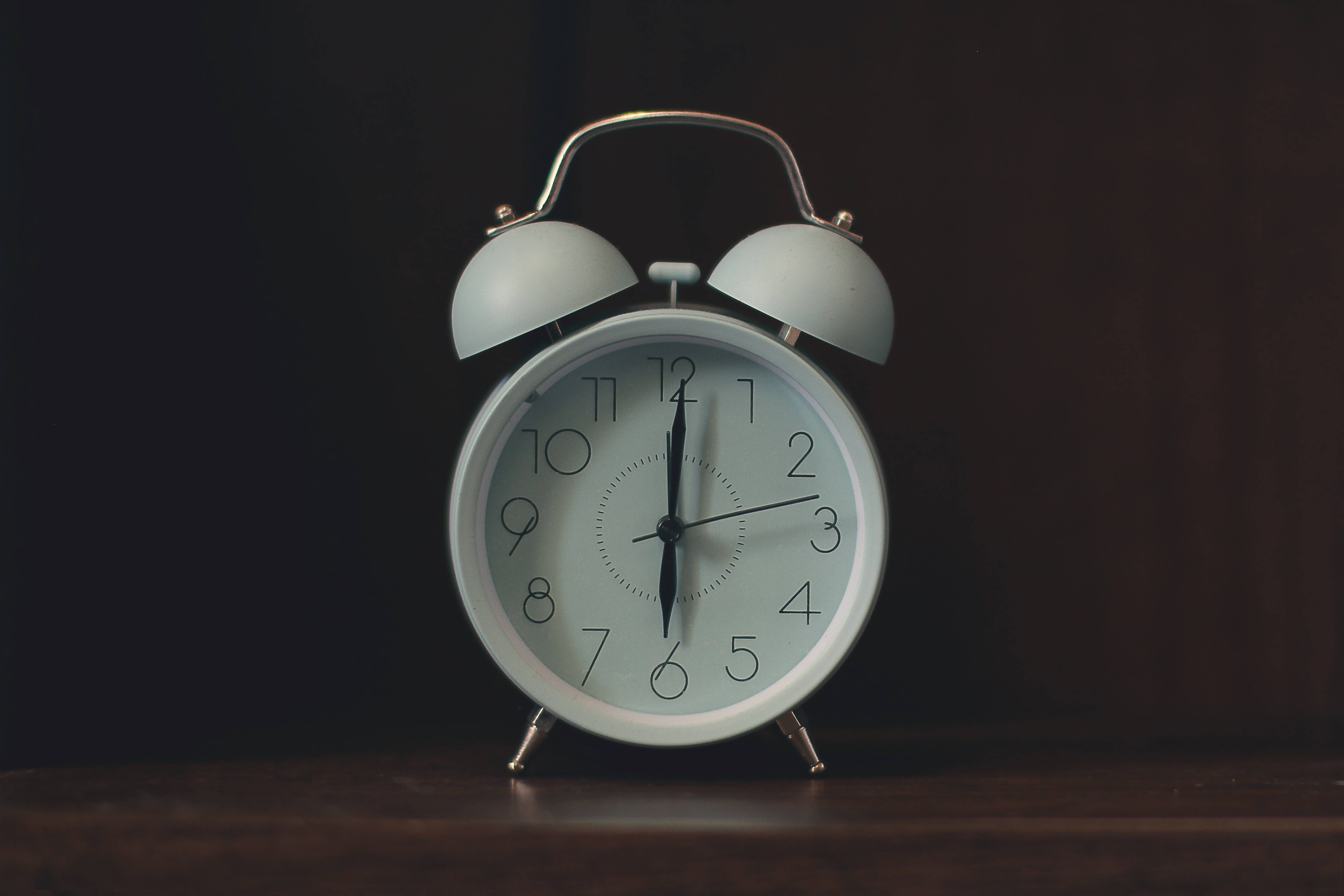 Clock 桌布 壁紙 — 一個復古白色鬧鐘，帶有雙鈴，放在木質表面上，背景為深色，指針指向十二點。