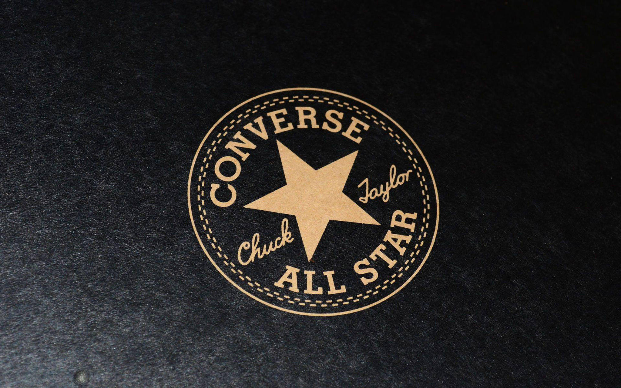 Converse Logo 桌布 壁紙 — 一個復古的 Converse Chuck Taylor All Star 標誌，以棕褐色呈現於帶有紋理的黑色布料上，並附有縫線邊緣細節。