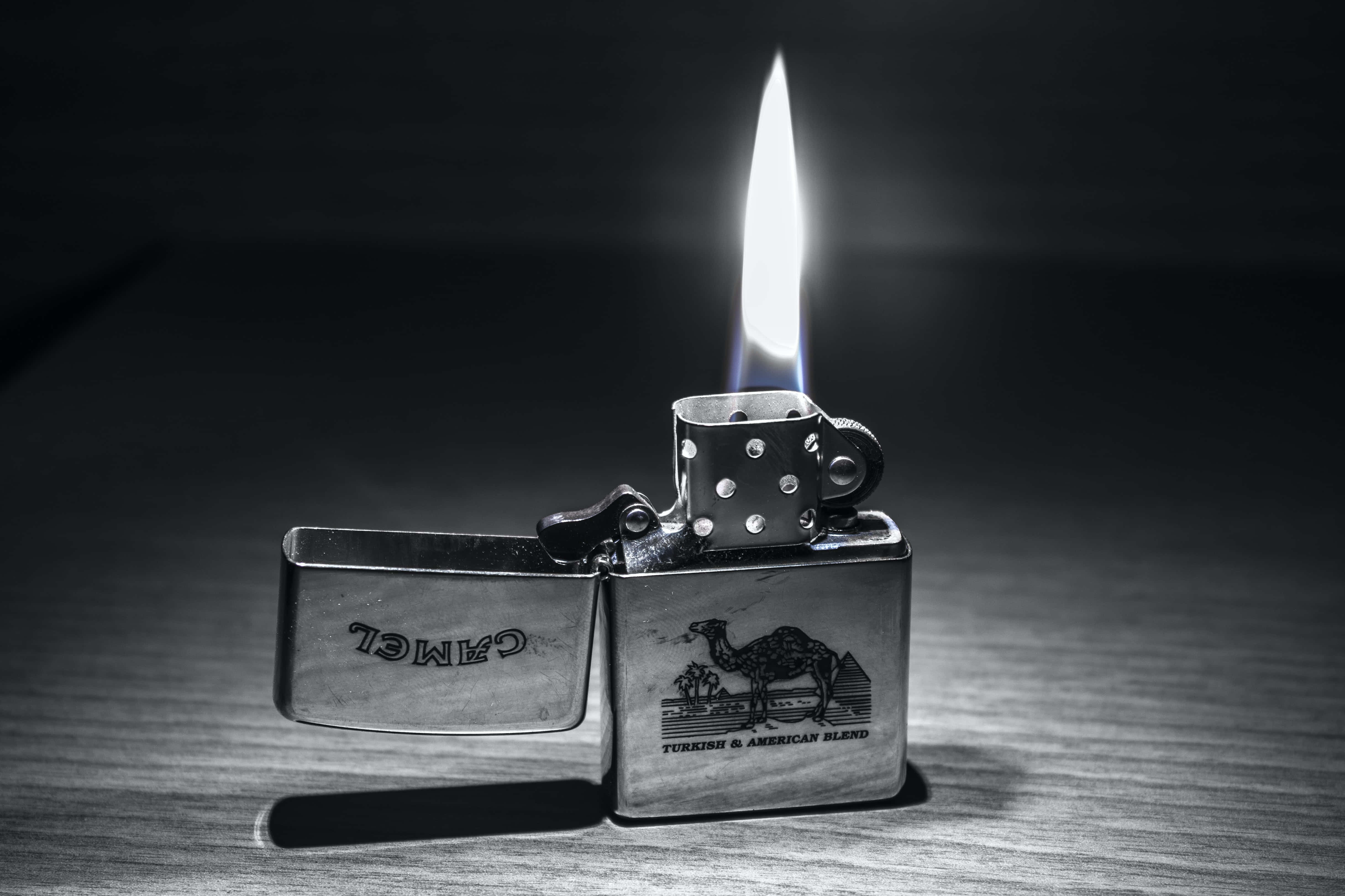 黑白 桌布 壁紙 — 一個復古的Camel打火機，在木質表面的黑暗背景下燃燒著明亮的火焰。