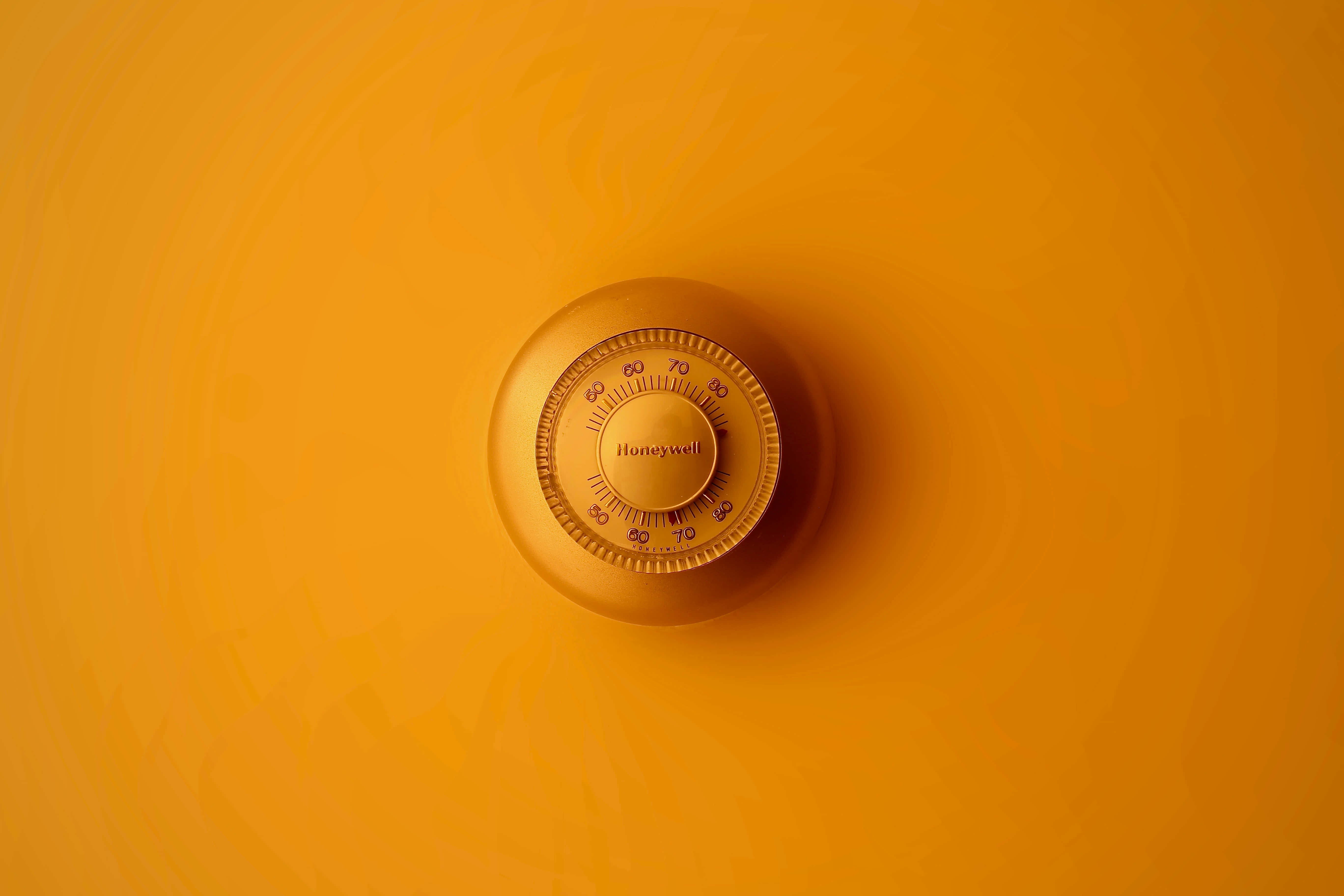 彩色動畫 桌布 壁紙 — 一個復古的Honeywell恆溫器置於溫暖的橙色漸變背景中央，光線柔和。