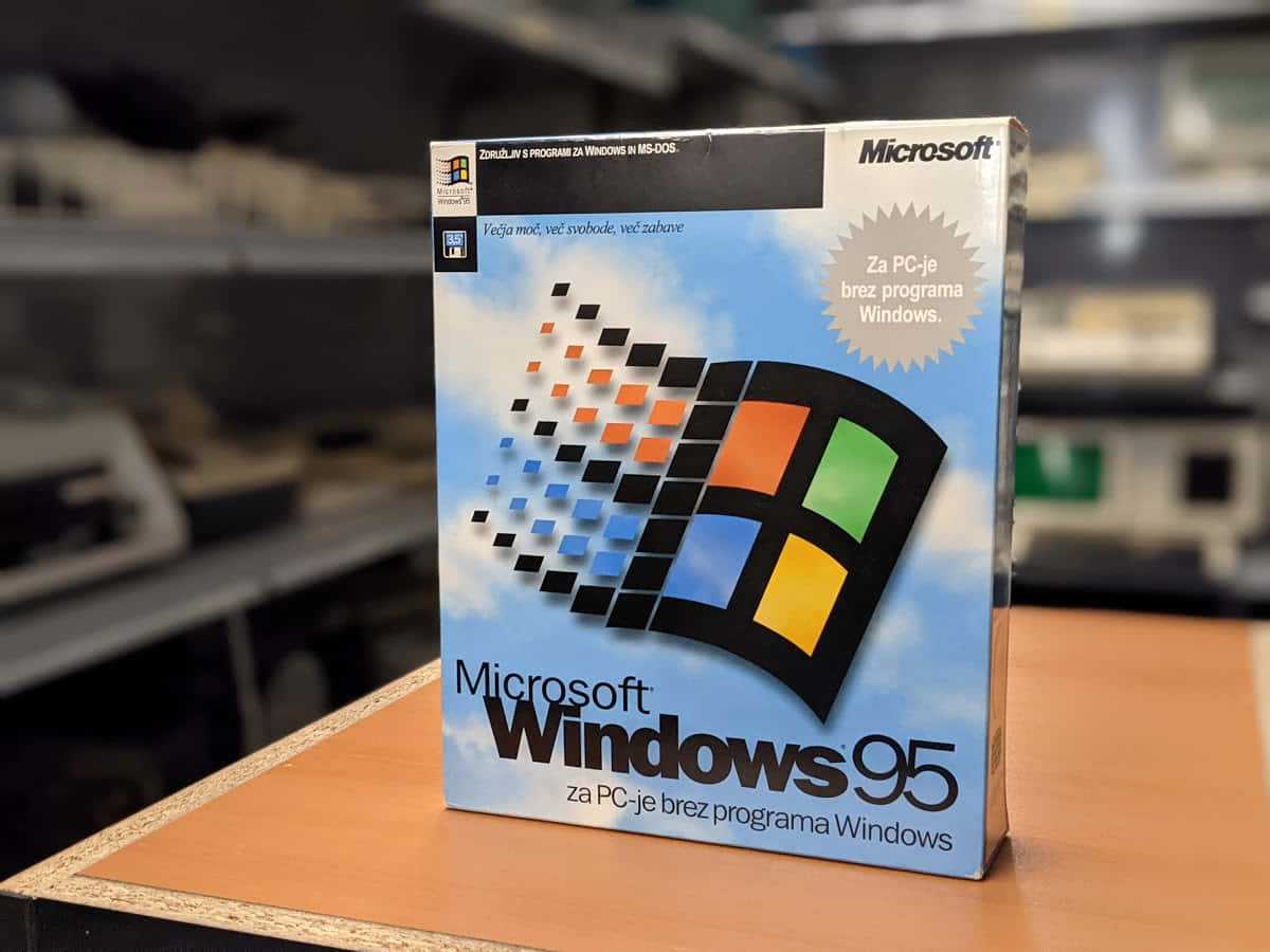 Windows 95 動態圖 桌布 壁紙 — 一個復古的Microsoft Windows 95軟體盒直立於木質表面上，背景是模糊的科技工作坊。