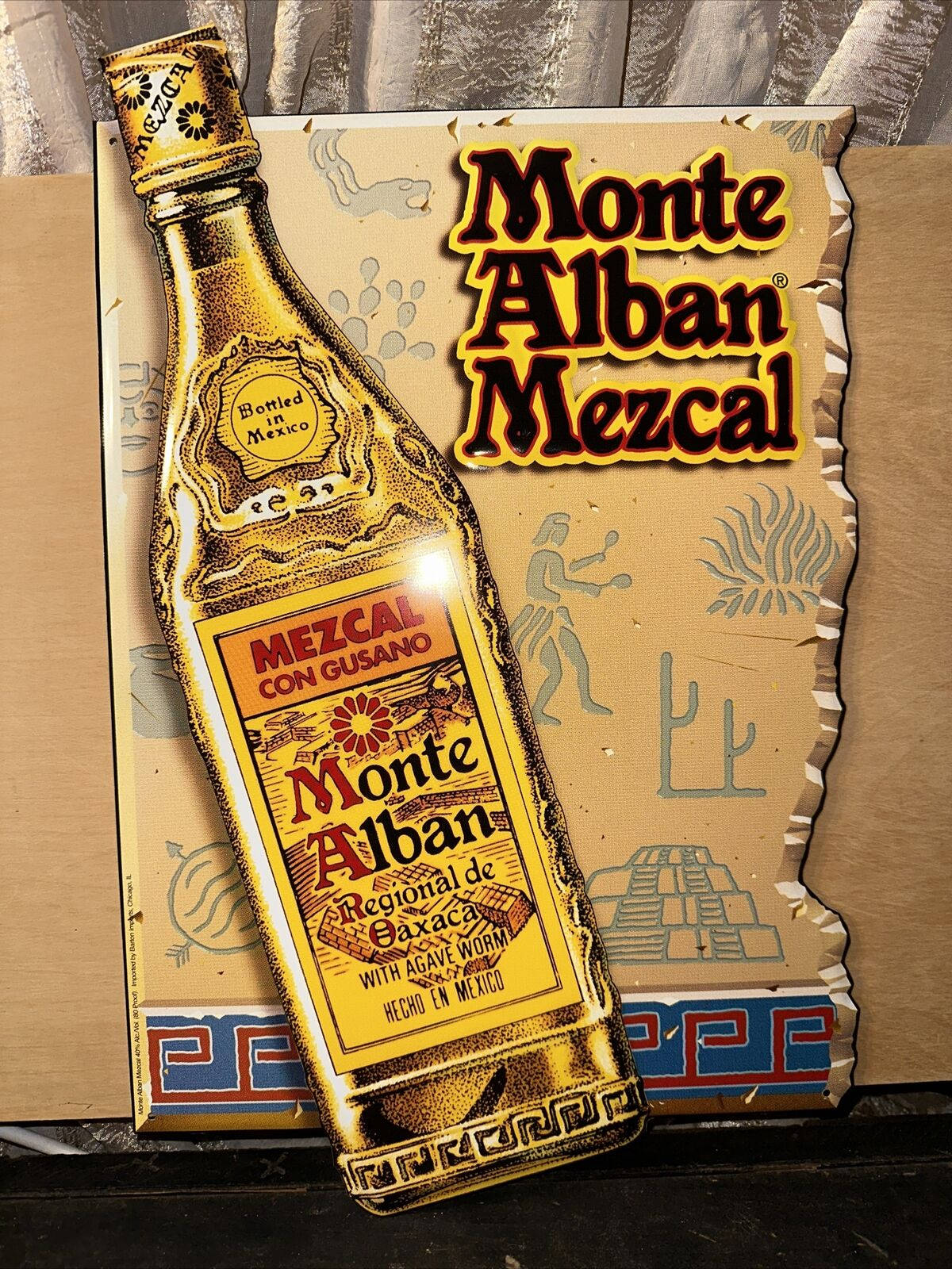 飲料 桌布 壁紙 — 一個復古的Monte Alban Mezcal酒瓶插圖，帶有金色點綴和墨西哥圖案，背景為紋理紙板。