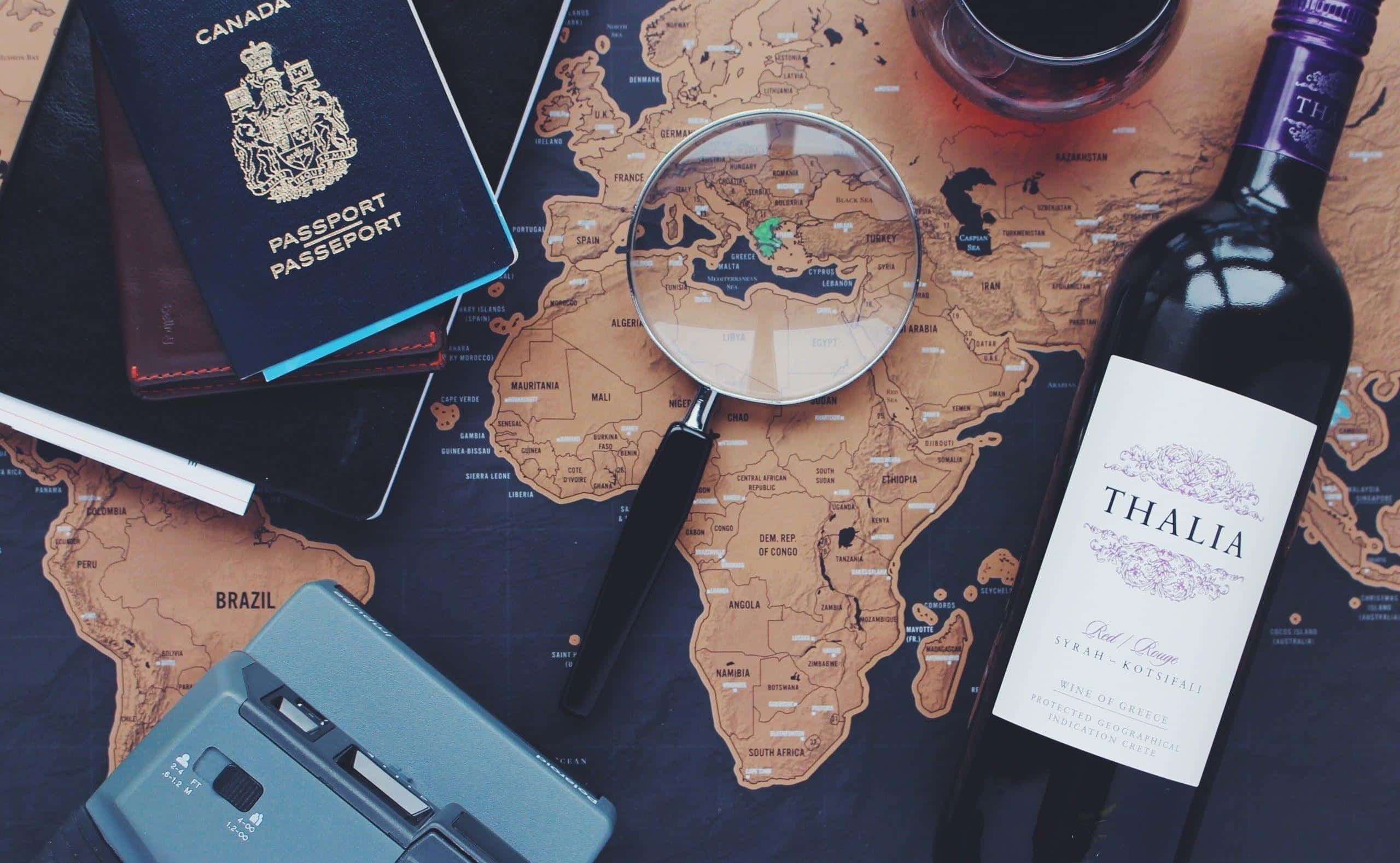 Passport 桌布 壁紙 — 一個復古相機護照和酒瓶放在世界地圖上，放大鏡懸浮在希臘上方。