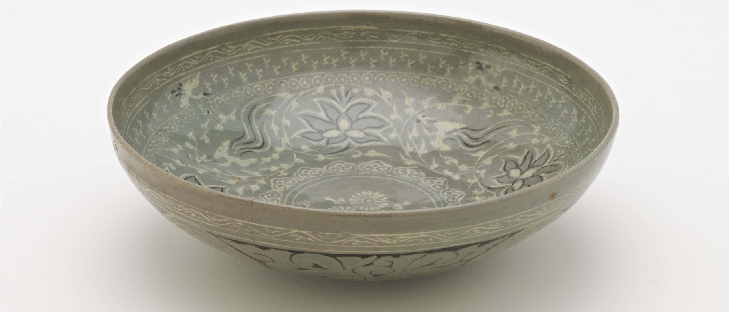 Ceramic 桌布 壁紙 — 一個復古綠色釉面陶瓷碗，在柔和的工作室燈光下帶有精緻的白色花卉和藤蔓圖案。