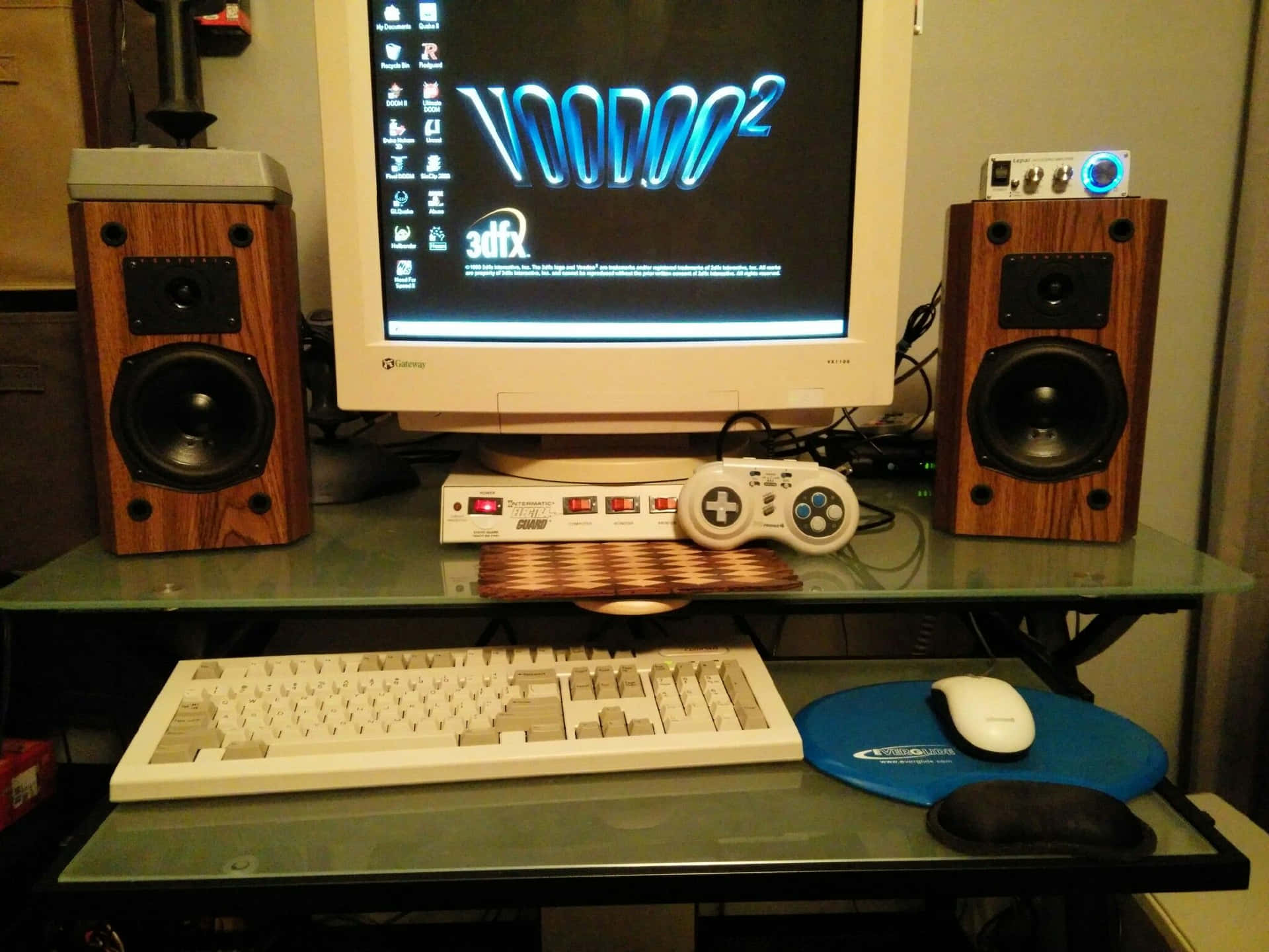 90s Computer 桌布 壁紙 — 一個復古遊戲設置，配備CRT顯示器，顯示藍色霓虹燈「Voodoo2」標誌，兩側是木製揚聲器。