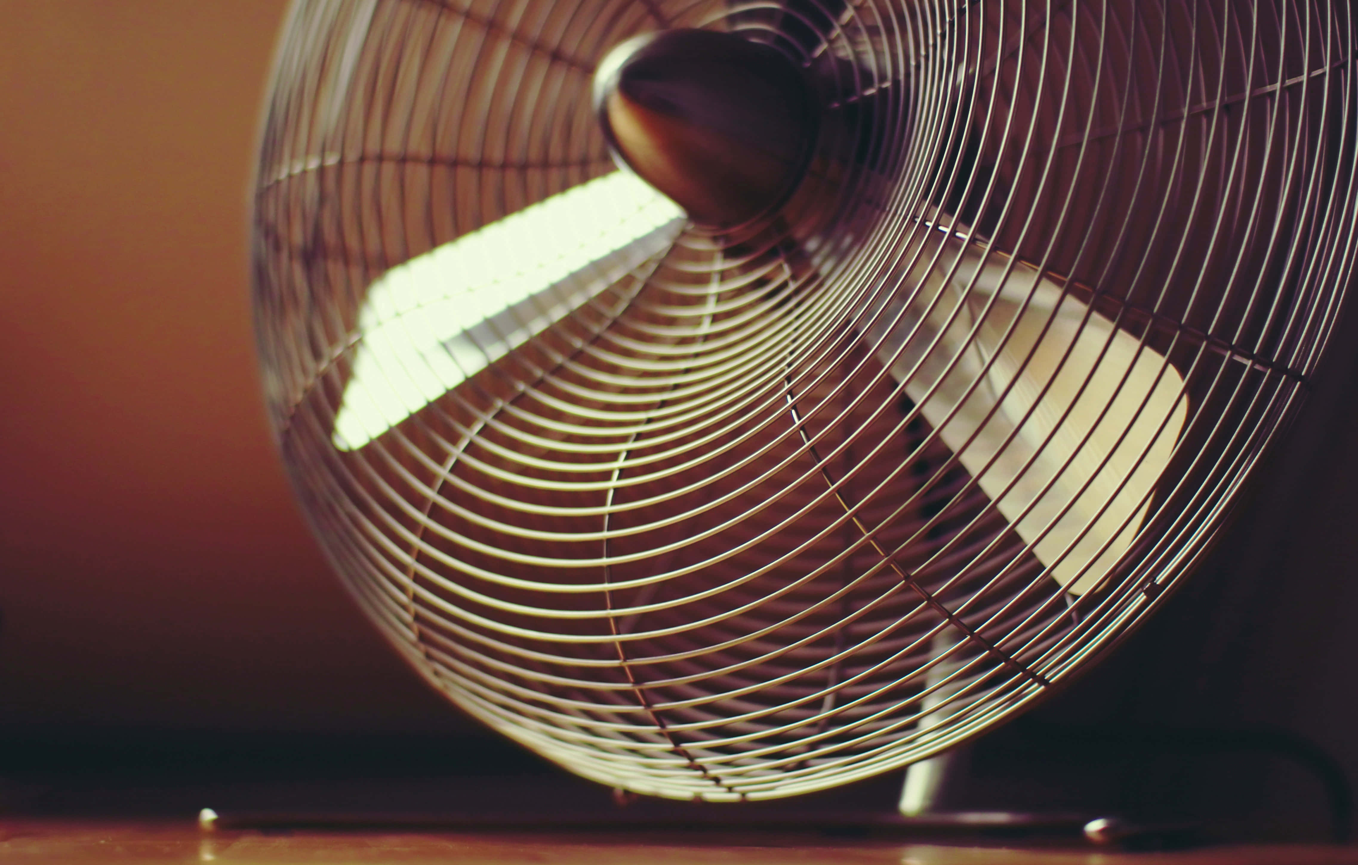 fan 桌布 壁紙 — 一個復古金屬風扇，帶有發光的葉片，在溫暖的琥珀色背景上柔和地旋轉。