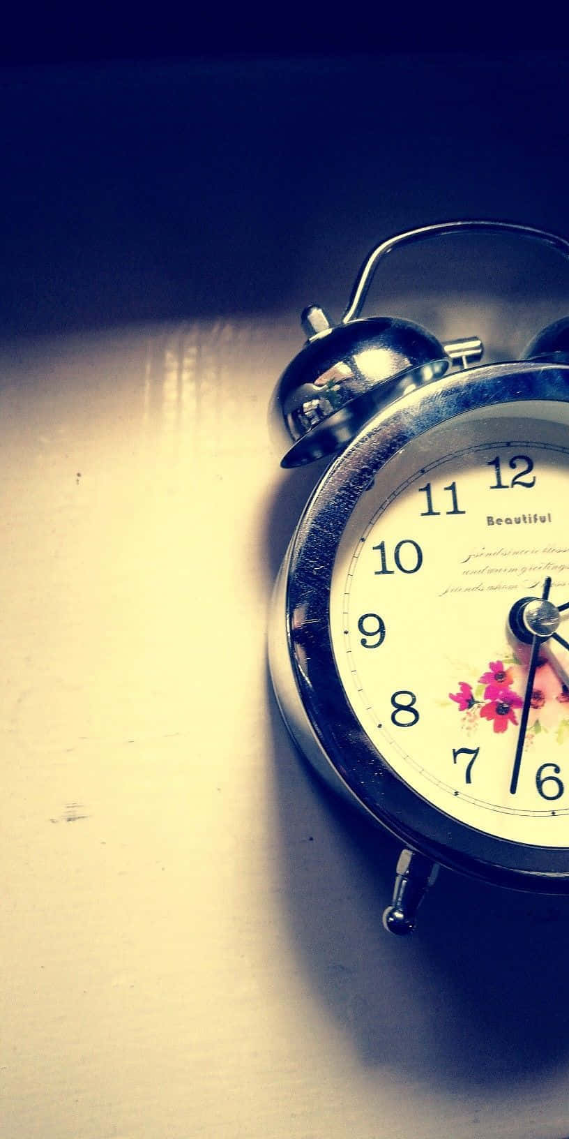 Time 桌布 壁紙 — 一個復古銀色鬧鐘，帶有花卉圖案錶盤，放置在陽光照射的木質表面上，投下柔和陰影。
