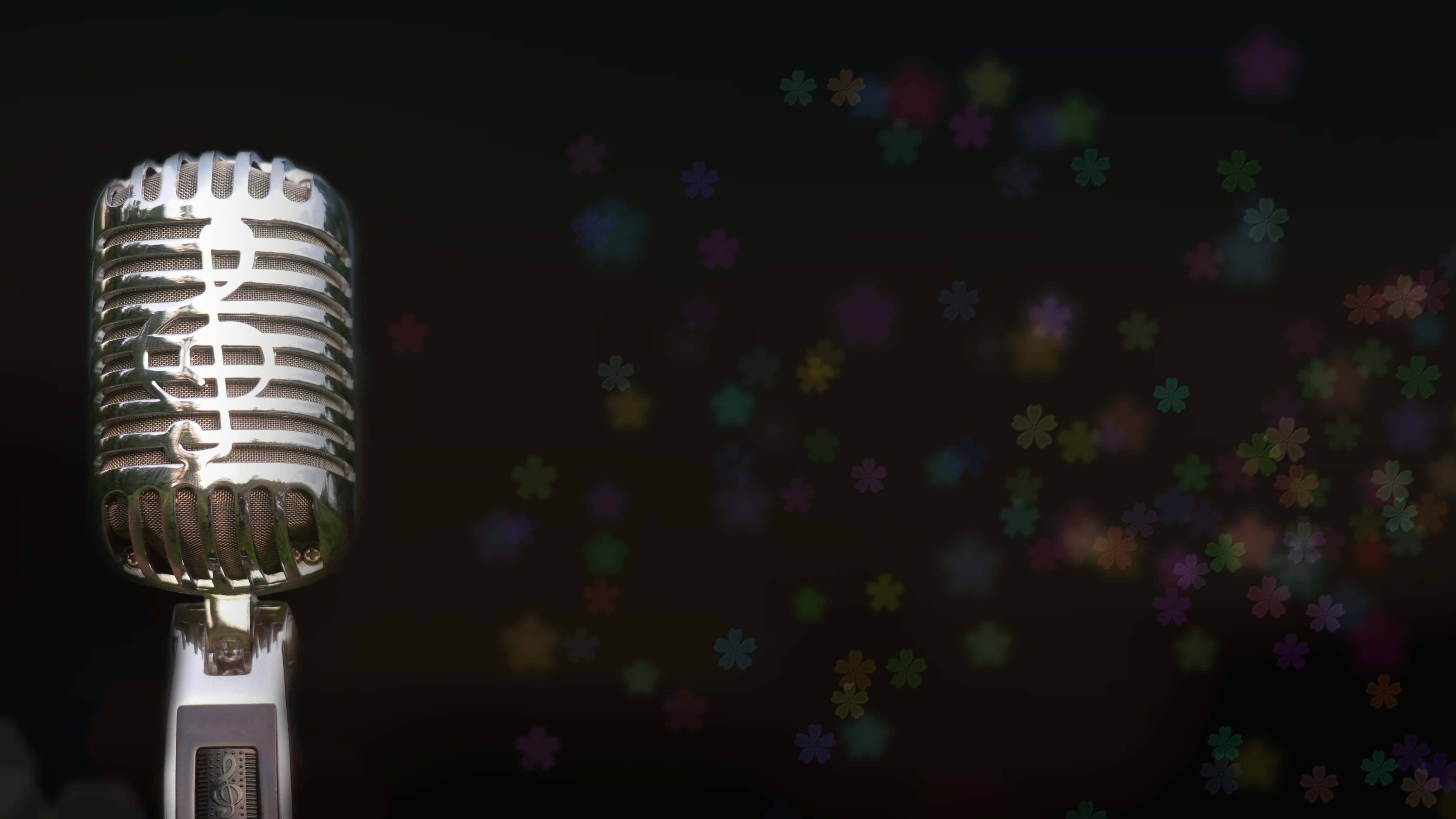 Singer 桌布 壁紙 — 一個復古銀色麥克風，格柵上刻有高音譜號，立在一個裝飾著色彩繽紛模糊花朵形狀的黑暗背景前。