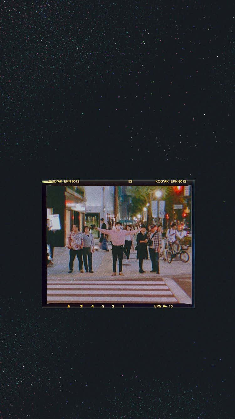 Aesthetic Grunge Phone 桌布 壁紙 — 一個復古電影畫面顯示一個人在夜晚的城市街道上張開雙臂，背景是星空。
