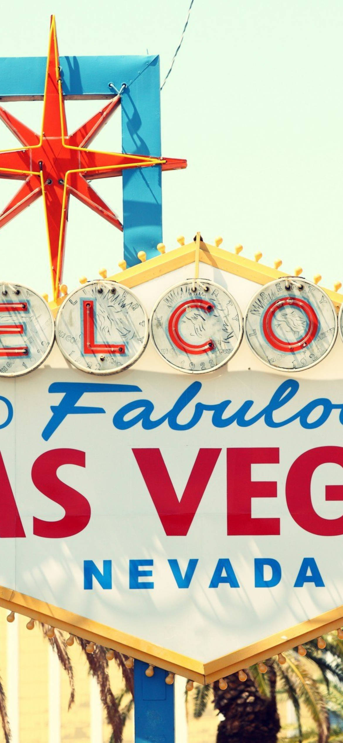 Vegas iPhone 桌布 壁紙 — 一個復古霓虹燈標誌以鮮豔的紅、藍、黃色在淡色天空下歡迎遊客來到內華達州拉斯維加斯。