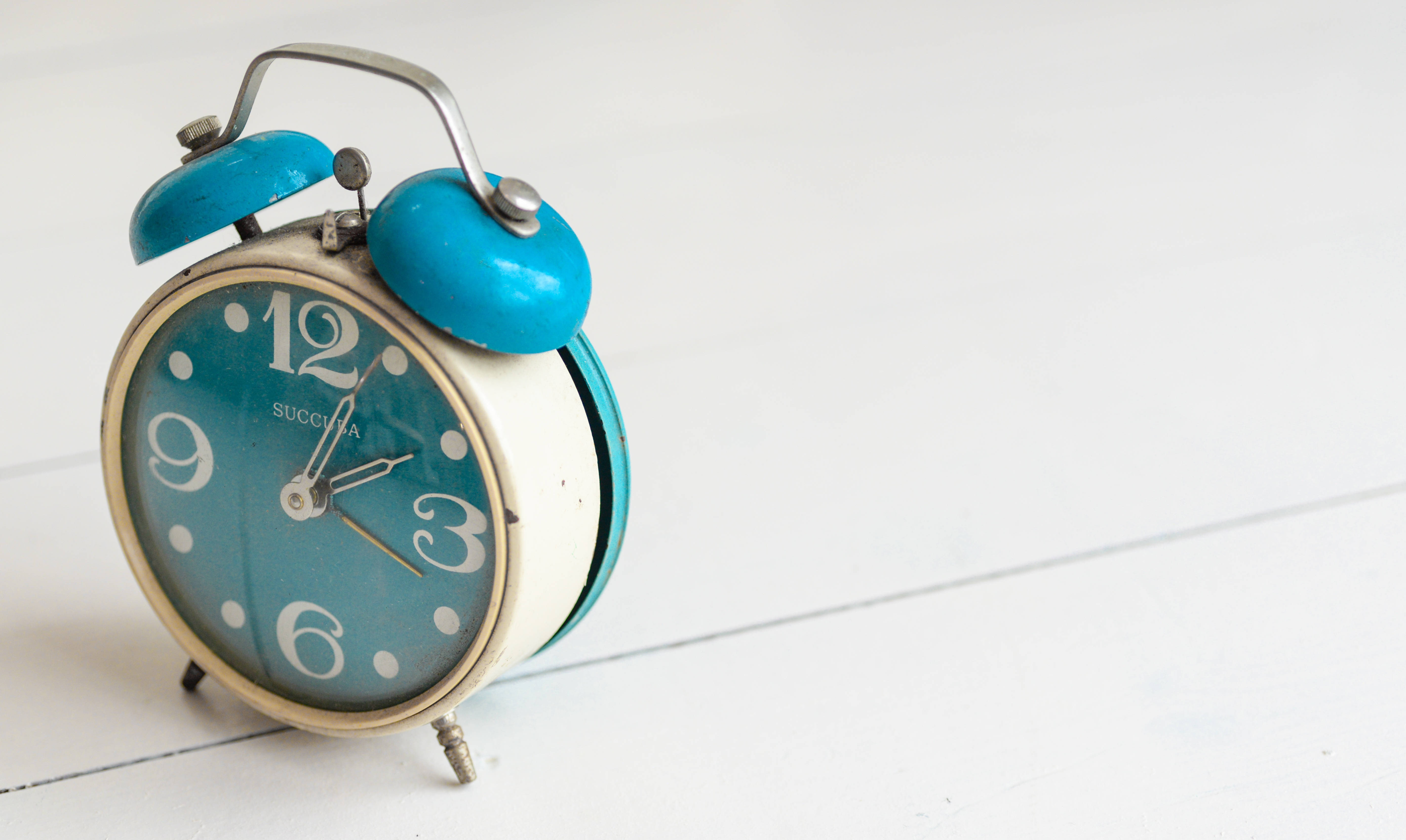 Clock 桌布 壁紙 — 一個復古青綠色鬧鐘，白色鐘面，放在明亮的白色木質表面上。