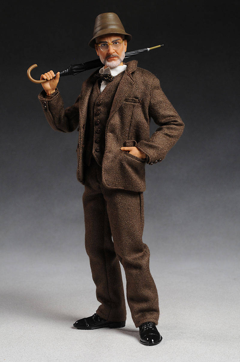 Indiana Jones 桌布 壁紙 — 一個復古風格的人體模型穿著棕色粗花呢西裝和帽子，在灰色漸變背景前拿著一把彎曲的雨傘。